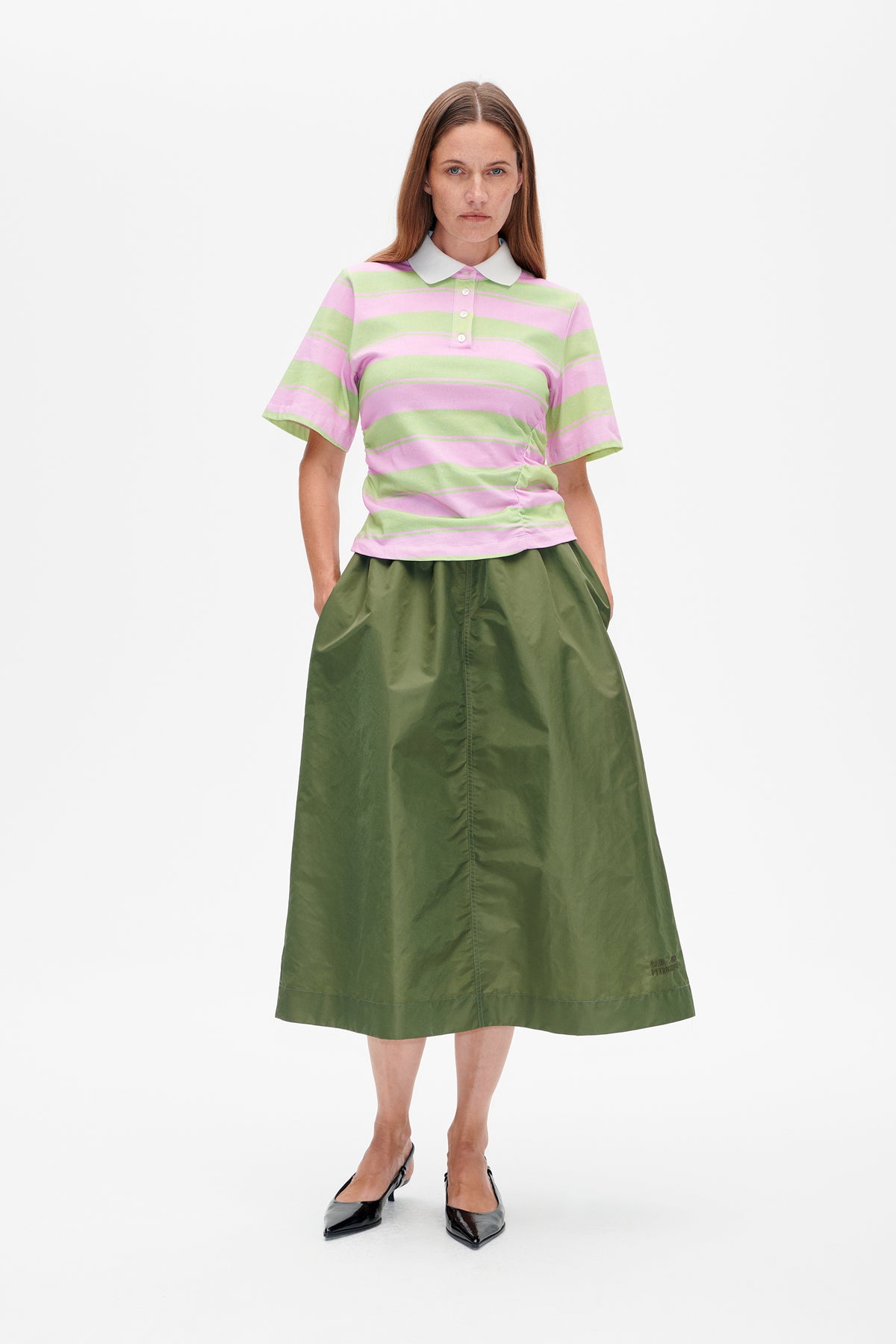Front view of a model wearing a pink and pale green striped polo shirt with a white collar and olive-green skirt.