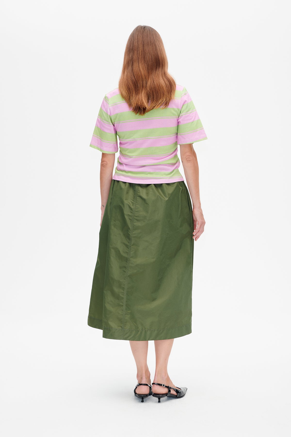 Back view of a model wearing a pink and light green striped short-sleeve T-shirt with a dark olive-green midi skirt.