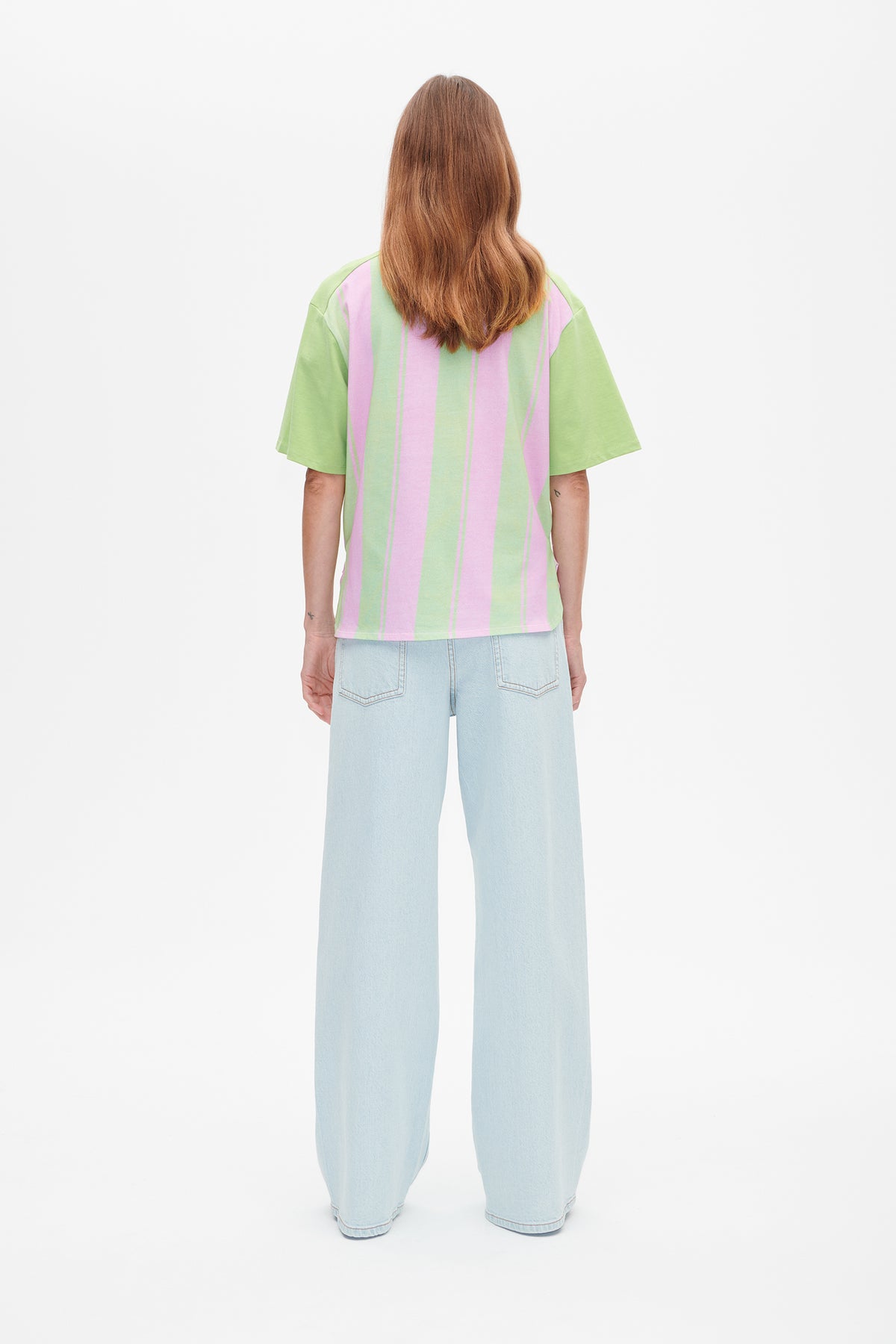 Rückenansicht eines kurzärmligen T‑Shirts mit breiten rosa- und hellgrünen Längsstreifen, kombiniert mit hellblauen Jeans mit weitem Bein.