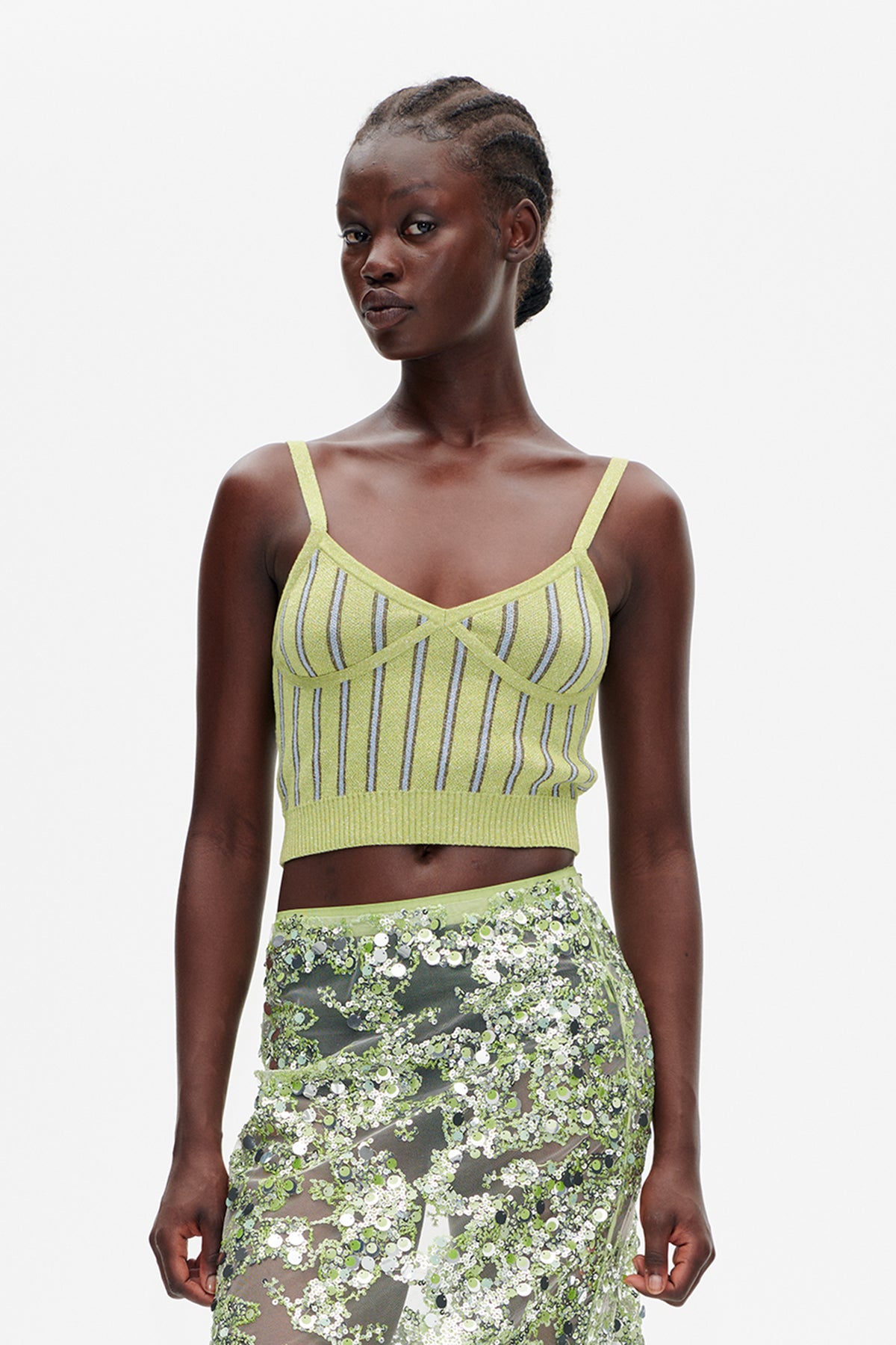 Model wearing a lime-green camisole crop top with vertical stripes and a sheer skirt densely decorated with green and silver sequins, front view.
