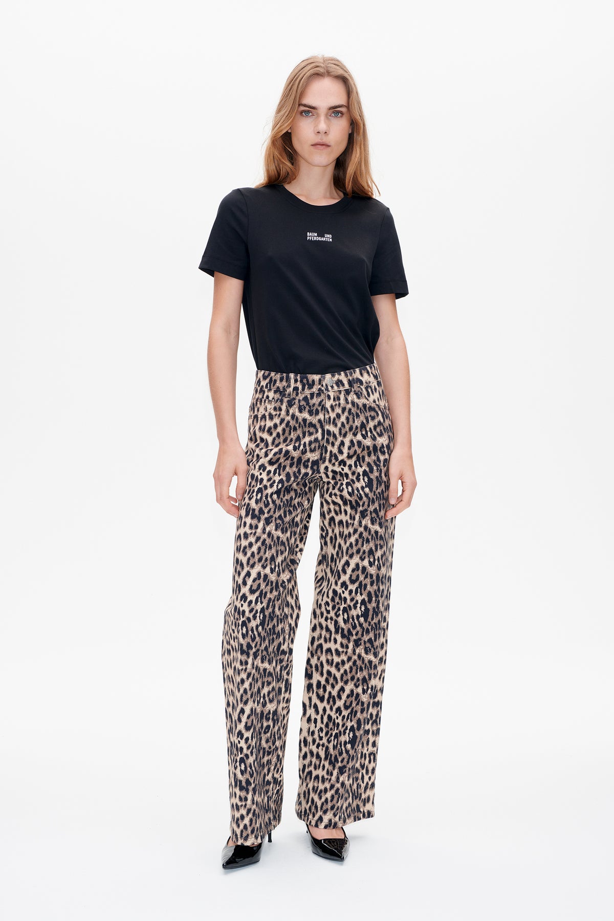 Model wearing a black crew-neck T-shirt with a small white chest logo and beige-and-black leopard-print wide-leg trousers.