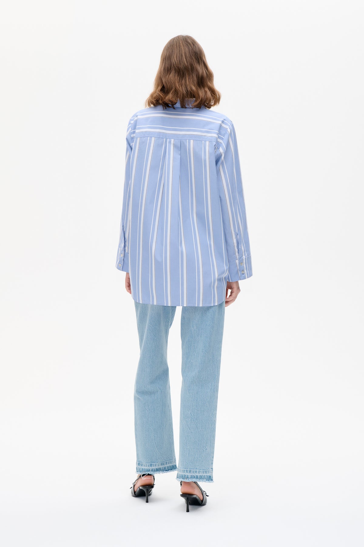 Rückenansicht einer langärmligen, hellblauen Bluse mit weißen Längsstreifen und einer horizontal gestreiften Passe, kombiniert mit hell gewaschenen Jeans.