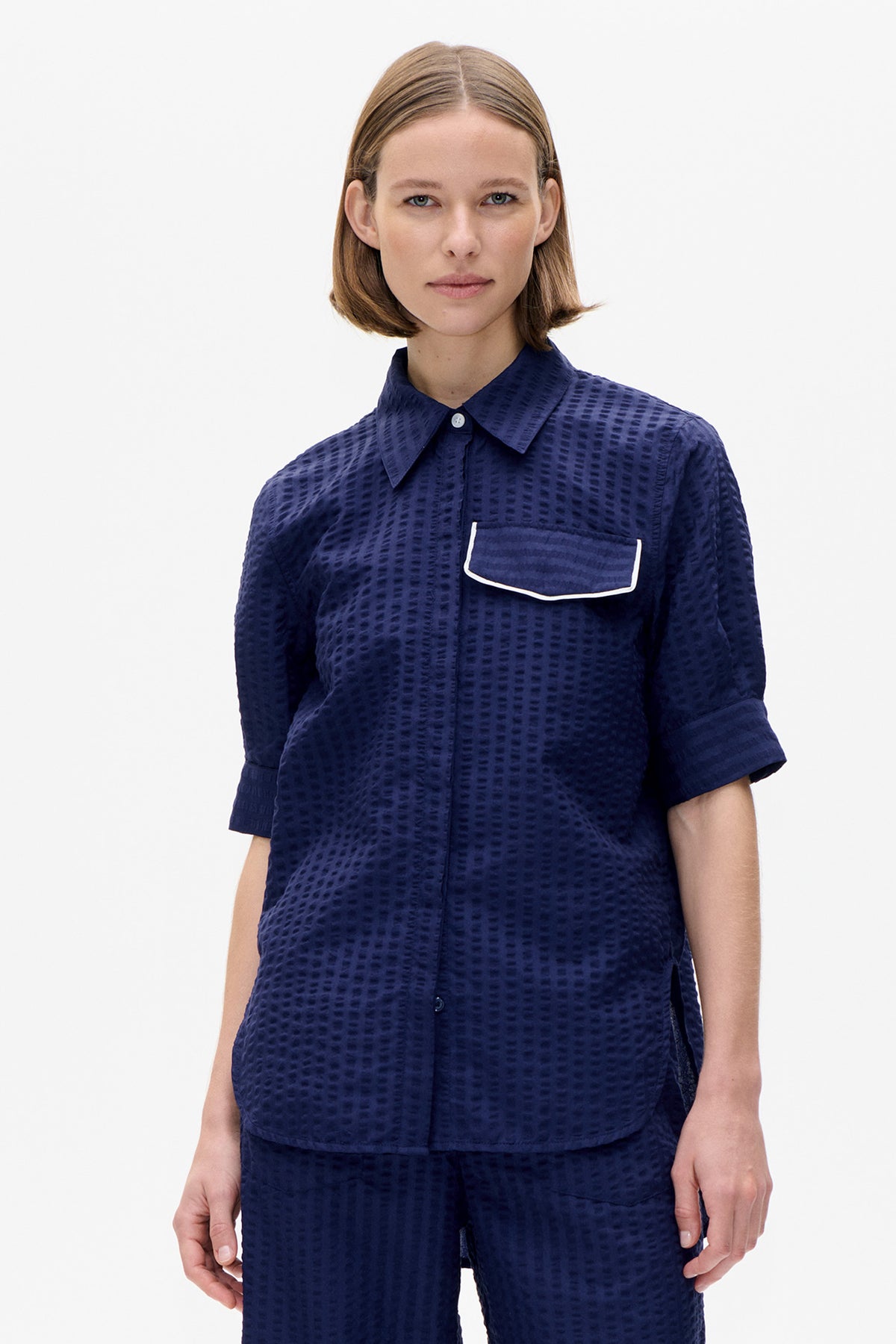 Front detail of a navy short-sleeved collared shirt with a raised dash pattern and a white-piped chest pocket.