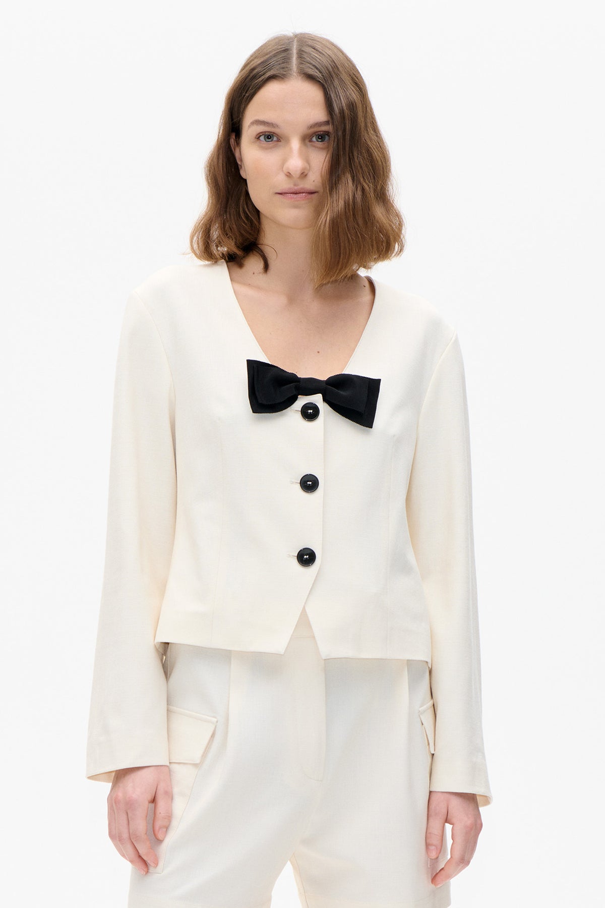 Front view of an ivory jacket with a deep V neckline, black bow detail and dark buttons.
