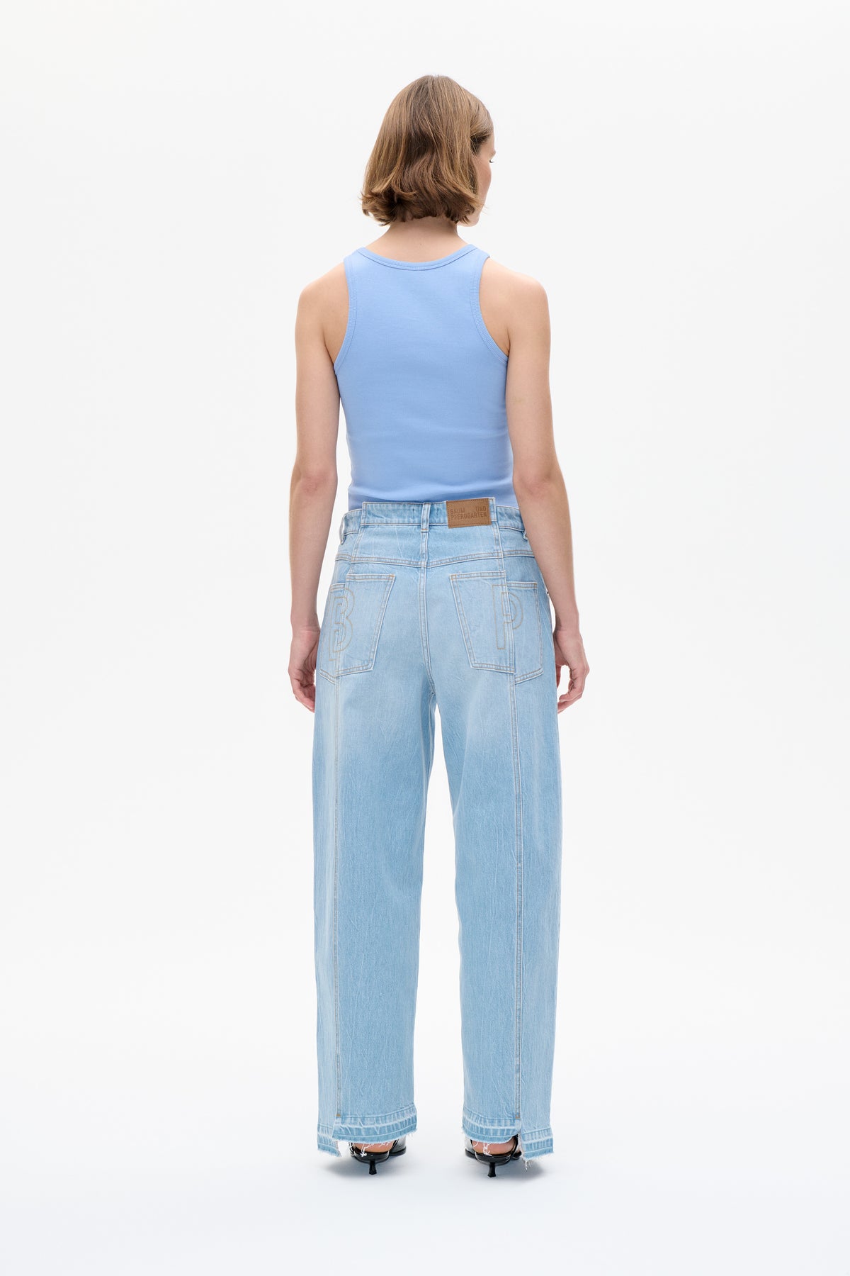 Back view of a model wearing a light blue ribbed sleeveless top and pale-wash wide-leg jeans with oversized outlined back pockets and frayed hems.
