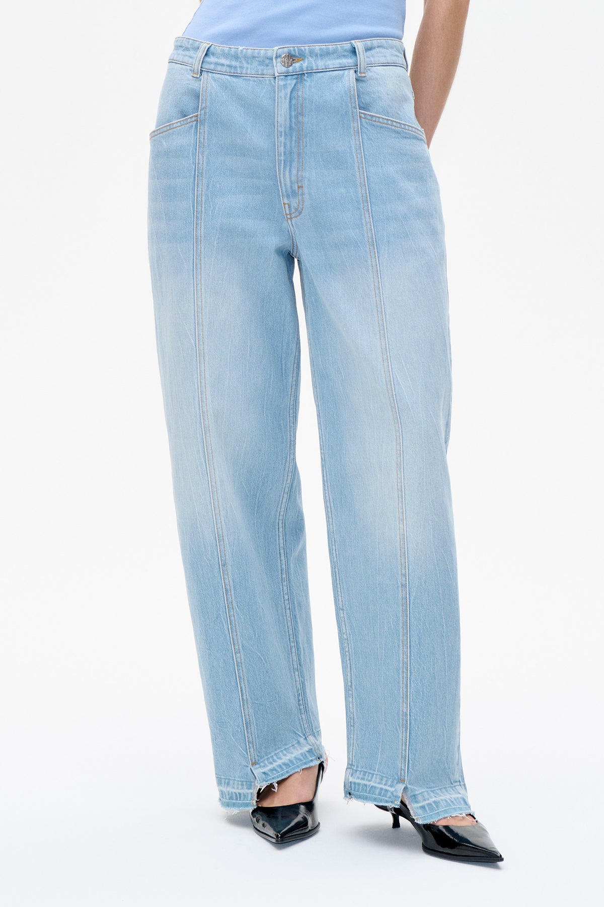 Front detail of light-wash blue jeans with wide legs, contrast stitching, a metal button and raw hems.