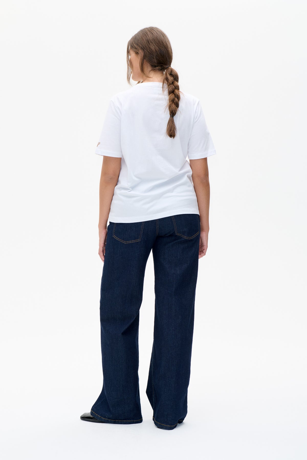 Back view of a white short-sleeved T-shirt with a small tan sleeve detail, paired with dark wide-leg jeans.