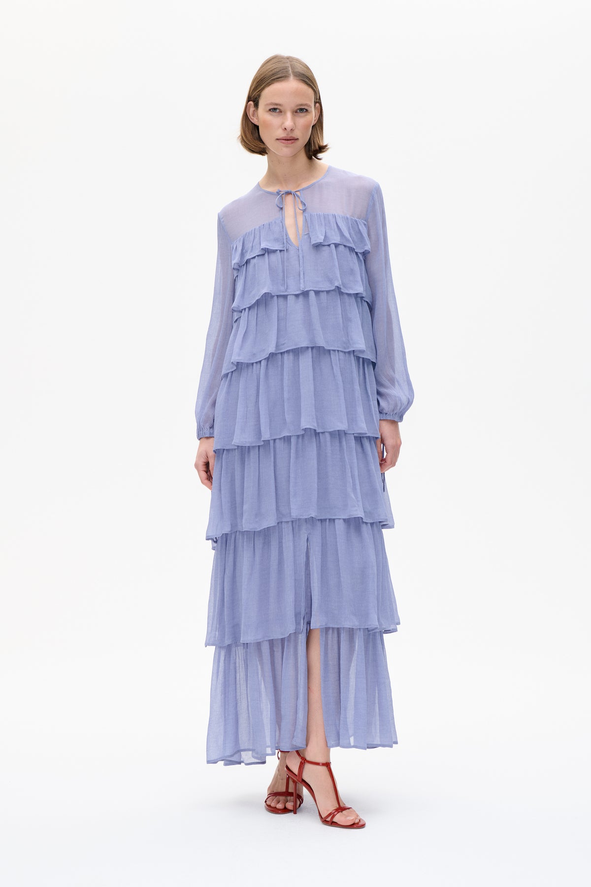 Front view of a model wearing a pale blue tiered dress with long sleeves, a tie neckline and layered ruffles.