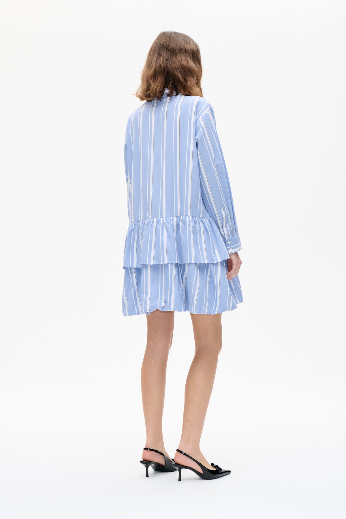 Back view of a model wearing a light blue and white vertically striped long-sleeve peplum blouse with matching shorts.