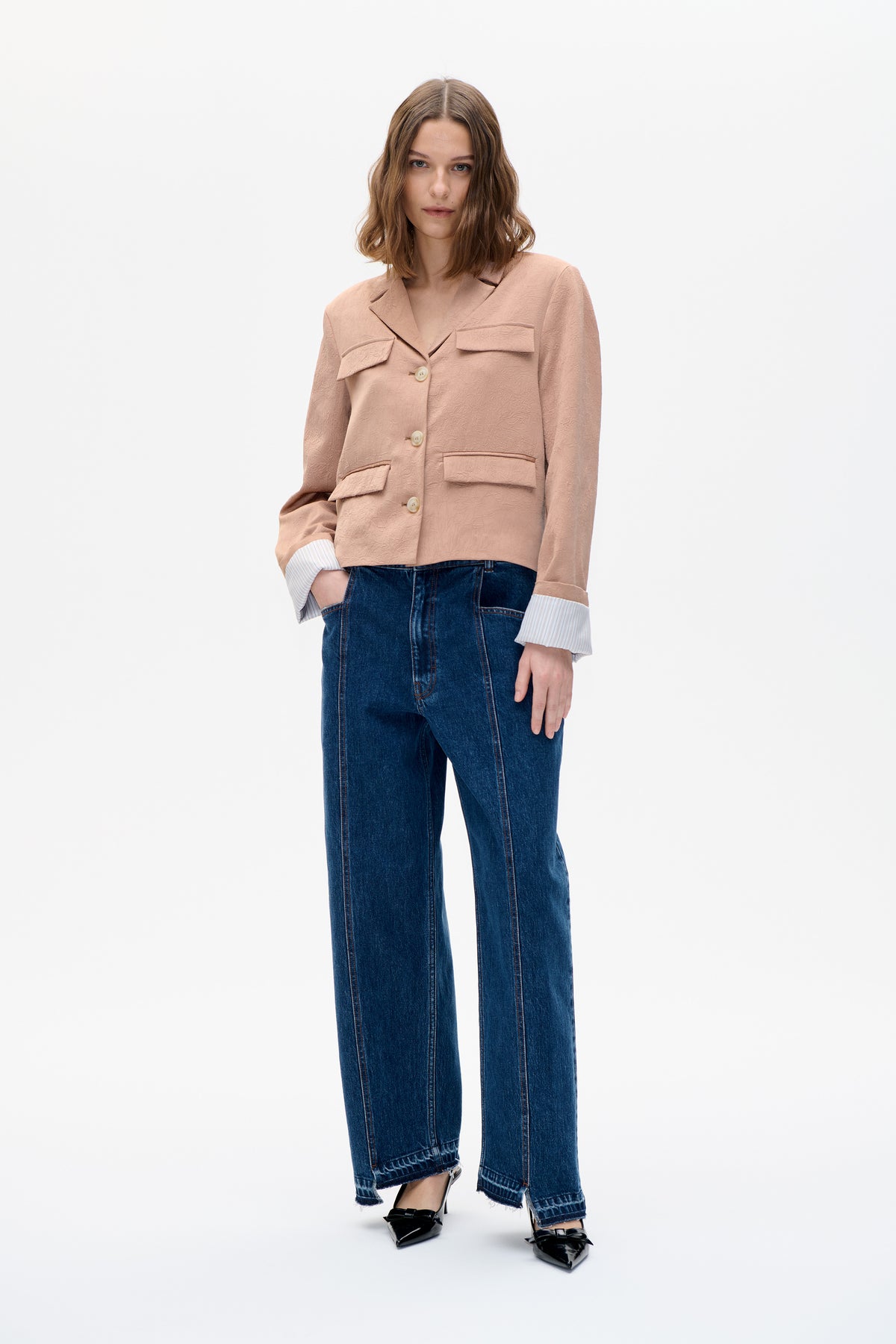 Model trägt einen zartrosa strukturierten Blazer mit Kerbkragen und Pattentaschen, kombiniert mit weit geschnittenen dunkelblauen Jeans.