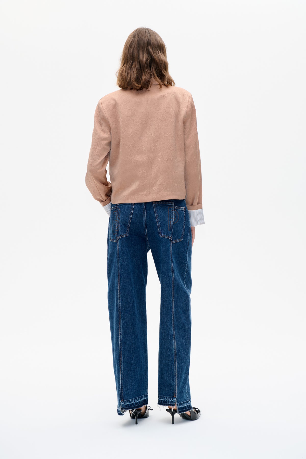 Rückenansicht eines Models in einem roséfarbenen Langarmtop mit geprägter, gekräuselter Struktur und dunkelblauen, weit geschnittenen Jeans.