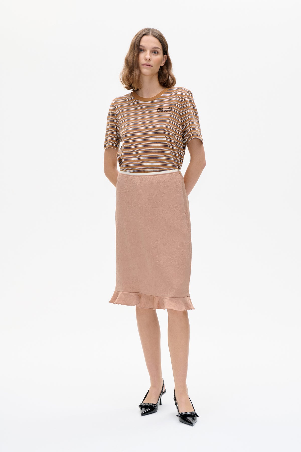 Model wearing a tan striped short-sleeve T-shirt with a small chest logo and a dusty pink textured skirt with a ruffled hem.