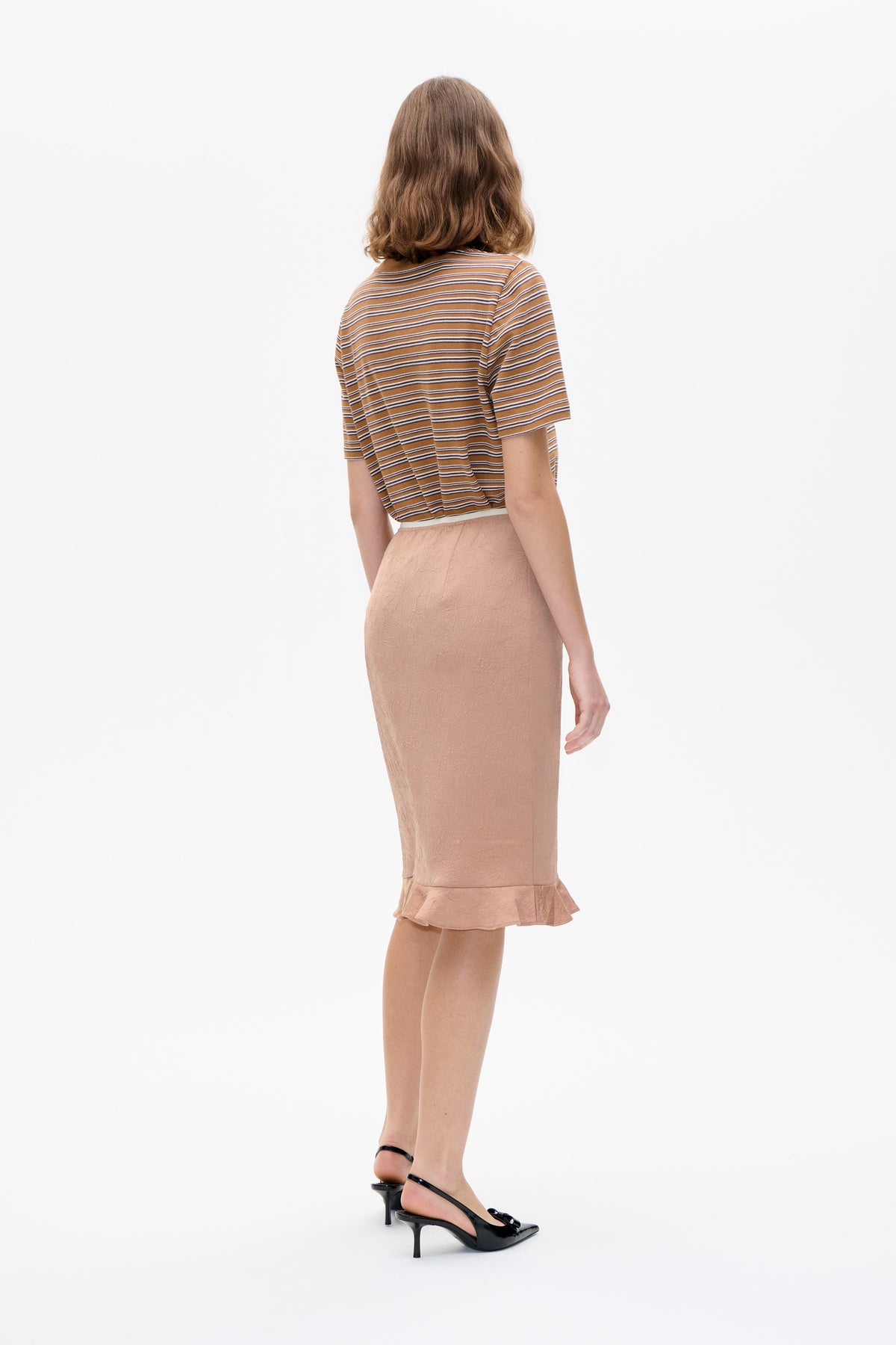 Back view of a model wearing a caramel-brown short-sleeved top with narrow cream and dark stripes, paired with a blush textured skirt.