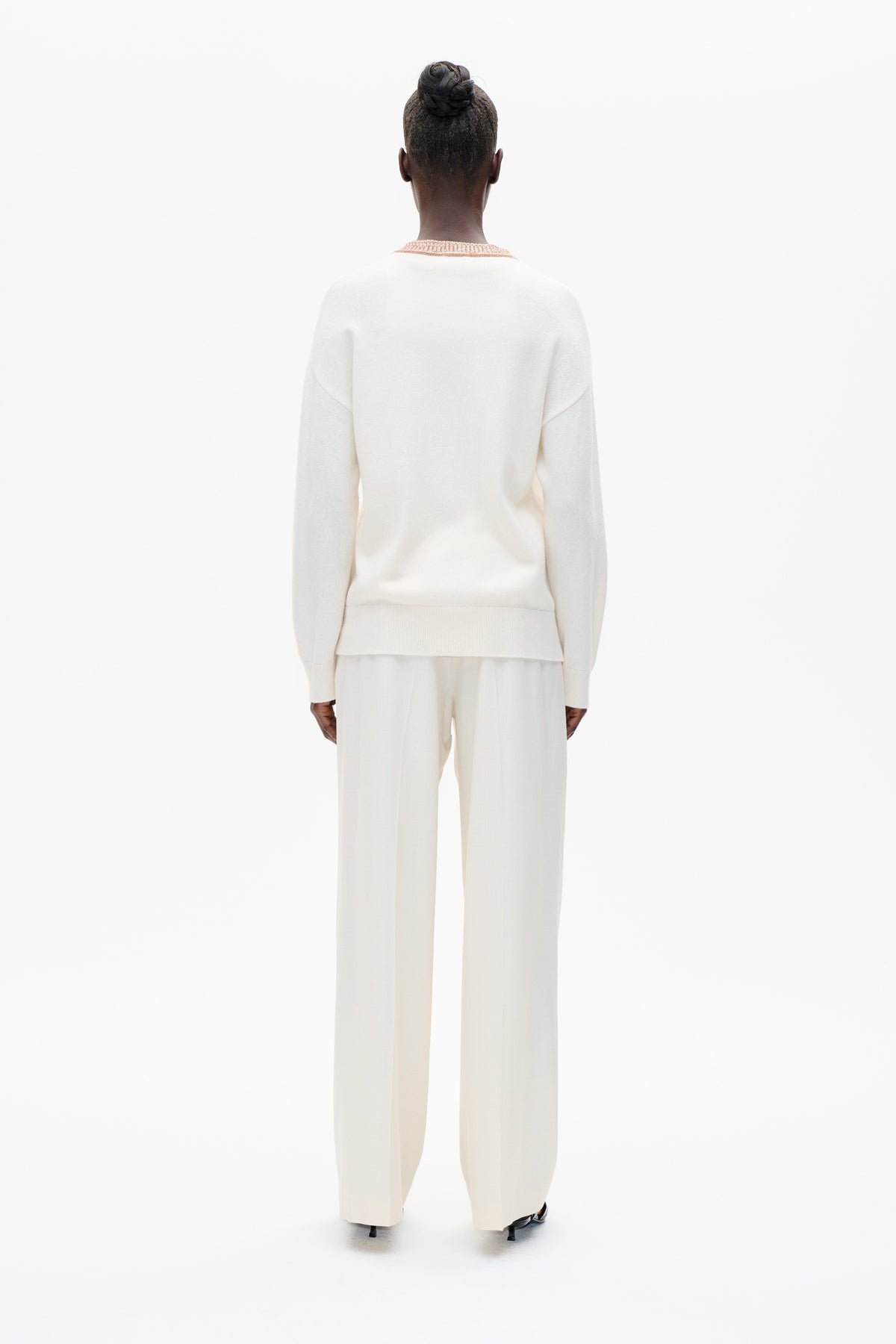 Rear view of a model wearing an ivory knit sweater with peach patterned neckline trim and matching wide-leg trousers.
