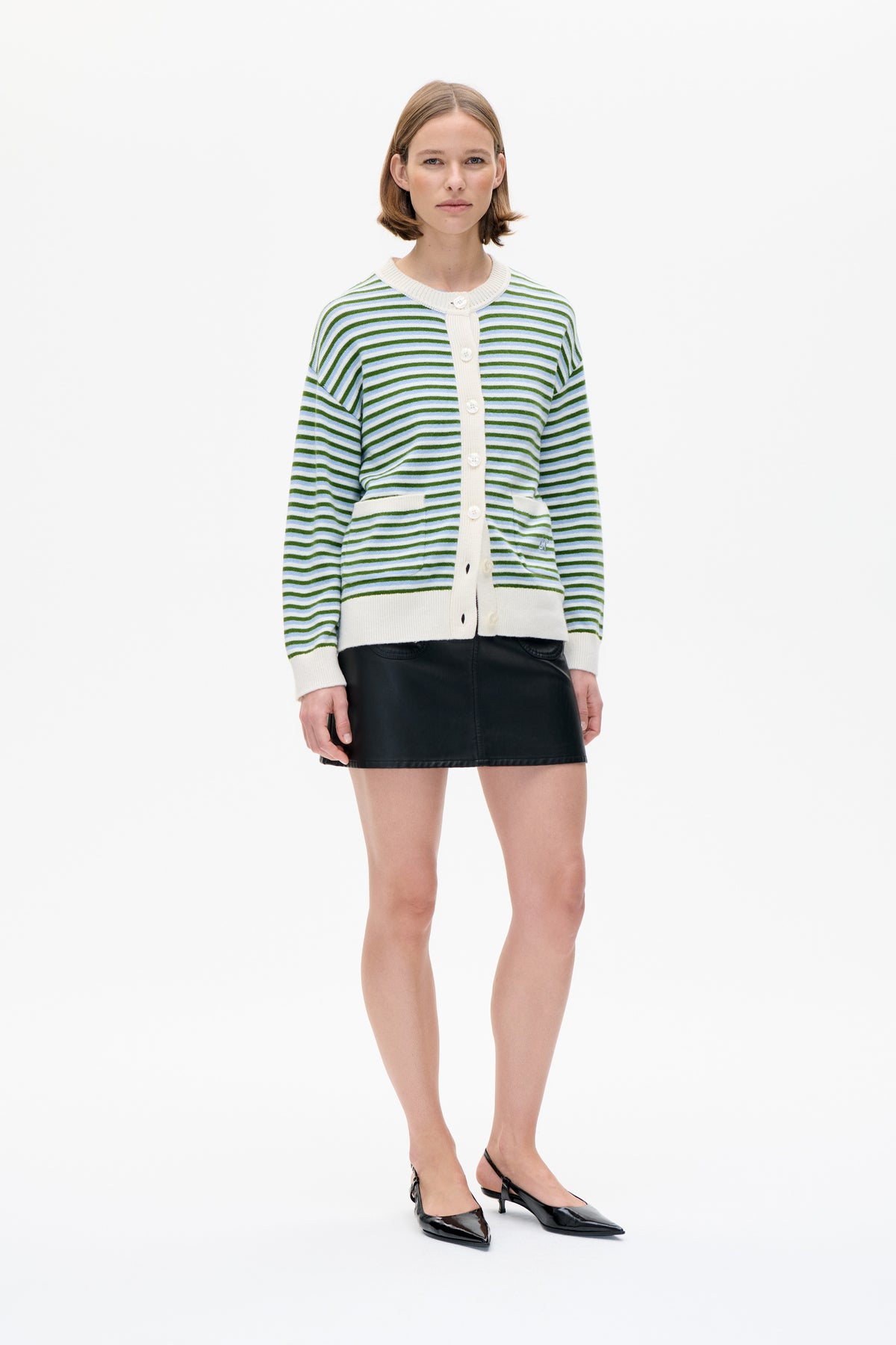 Vooraanzicht van een model met een cardigan met crèmekleurige bies en groene en lichtblauwe strepen, gecombineerd met een zwarte minirok en slingbacks met hak.