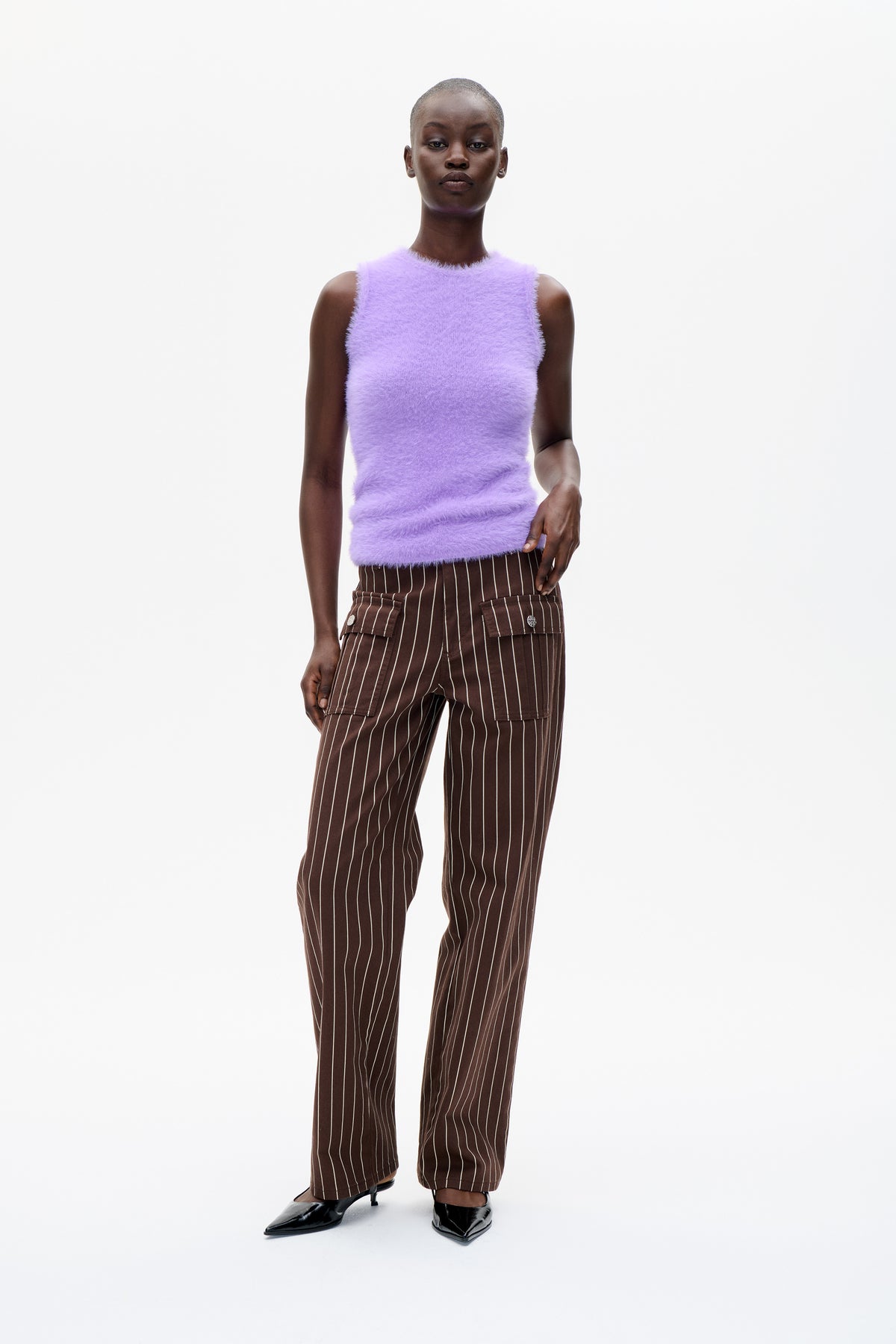Front view of a model wearing a fuzzy lilac sleeveless top with brown, cream-pinstriped cargo trousers.