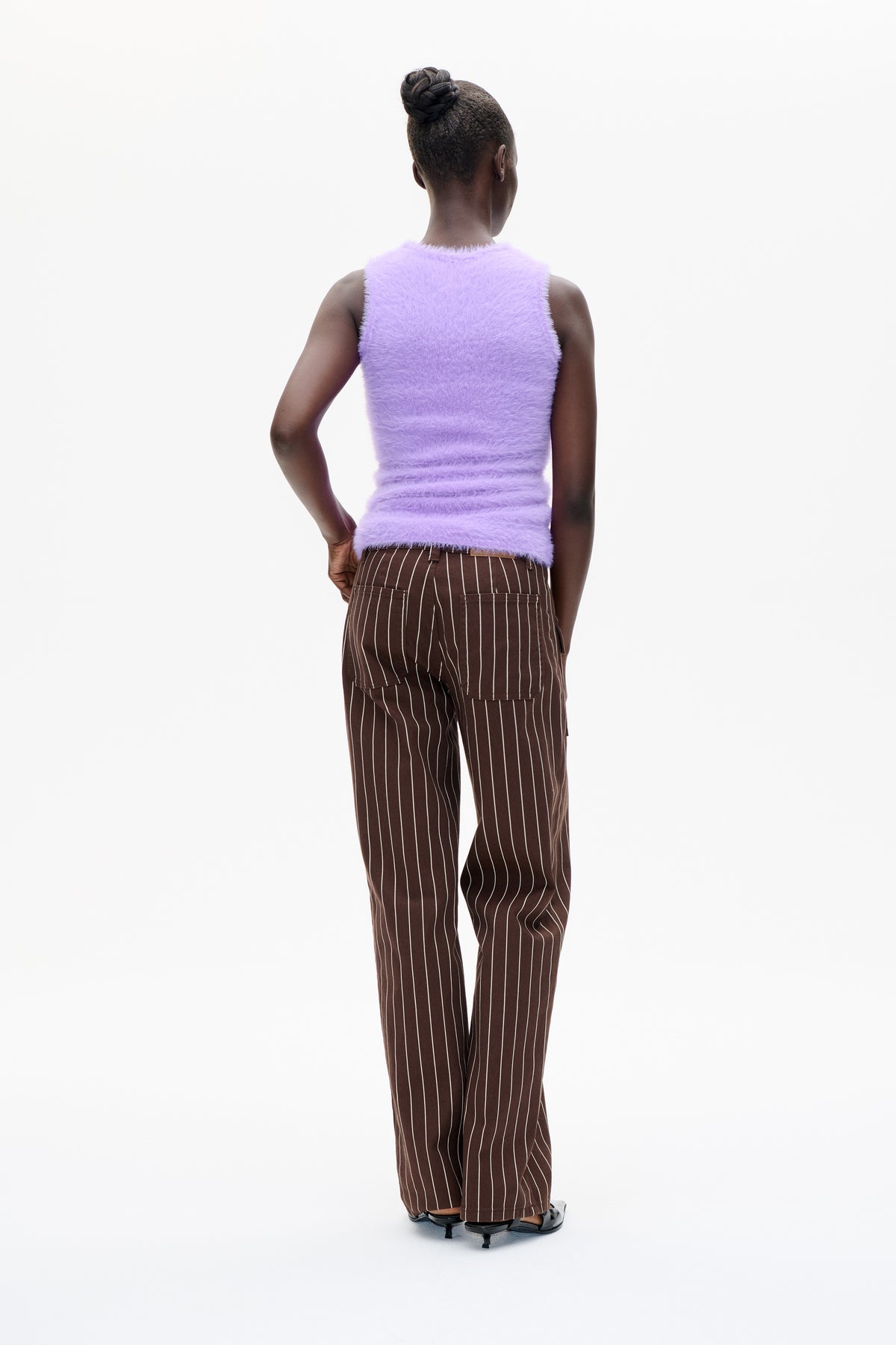 Back view of a model wearing a lilac fuzzy sleeveless top and brown trousers with thin white vertical stripes and patch pockets.