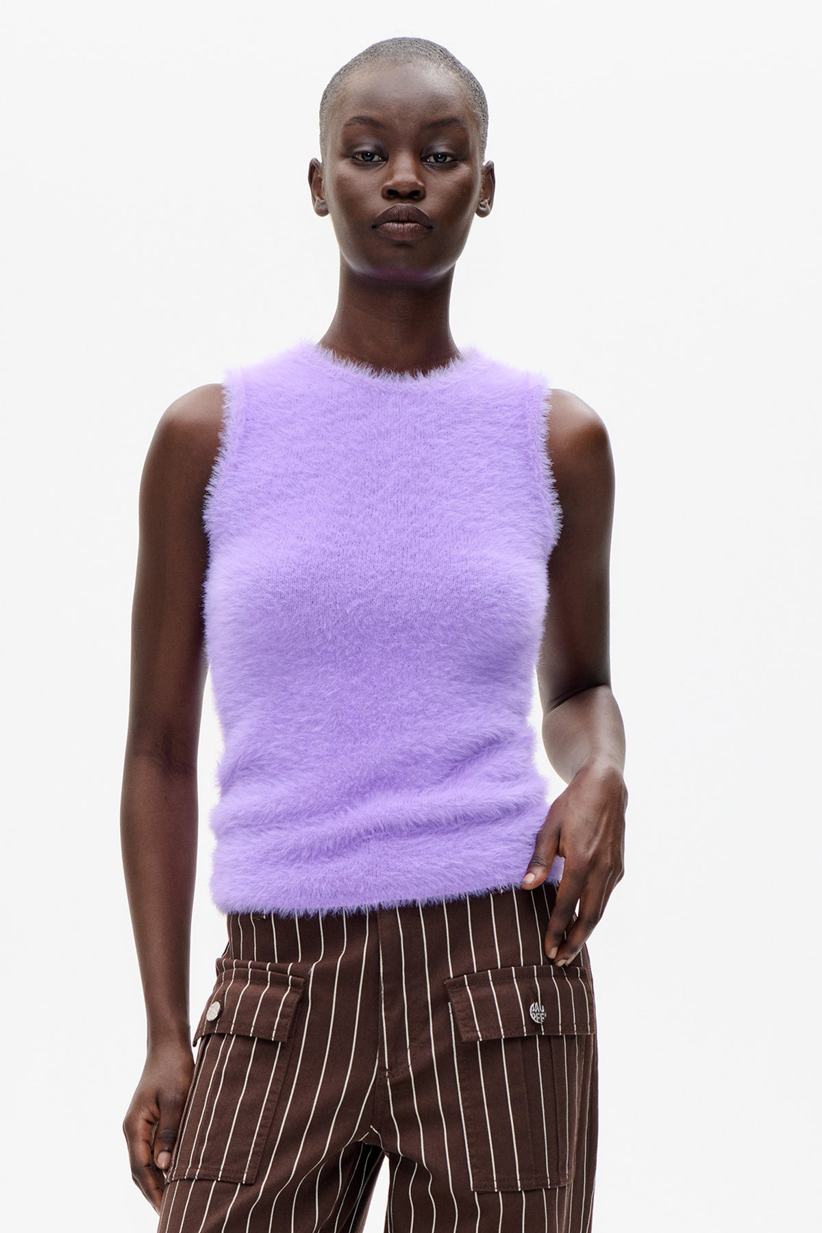 Front-facing model wearing a lilac fuzzy sleeveless top and brown trousers with cream pinstripes and flap cargo pockets.