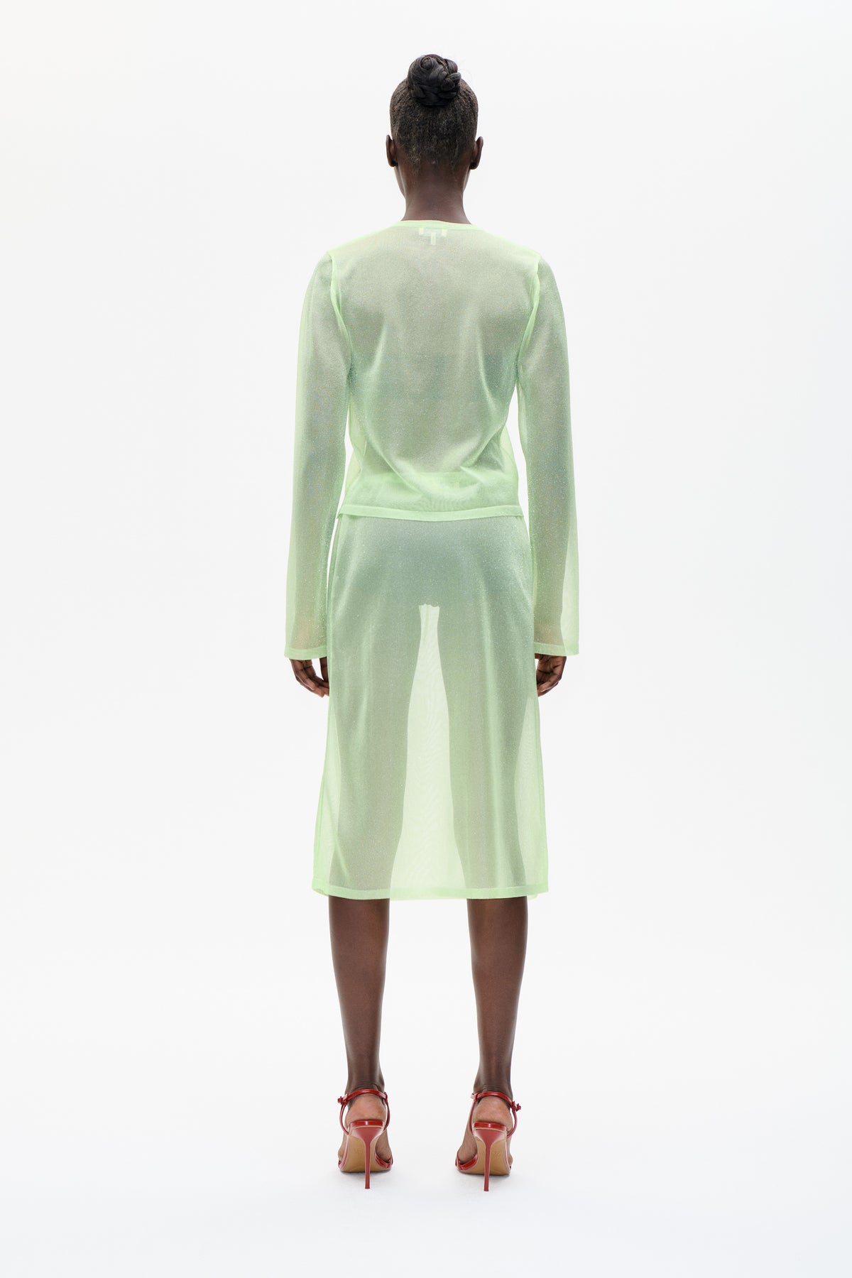 Back view of a model wearing a sheer, subtly shimmery pale green long-sleeved top and matching midi skirt
