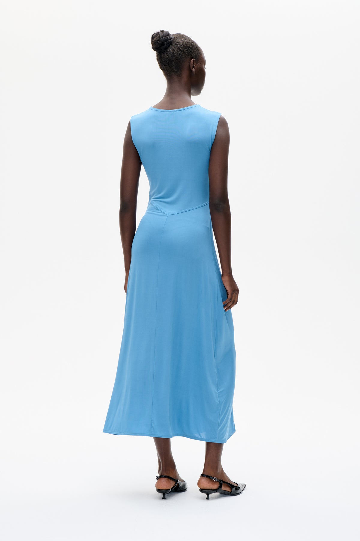 Model shown from the back wearing a sleeveless sky-blue midi dress with an angled waist seam and flared skirt.