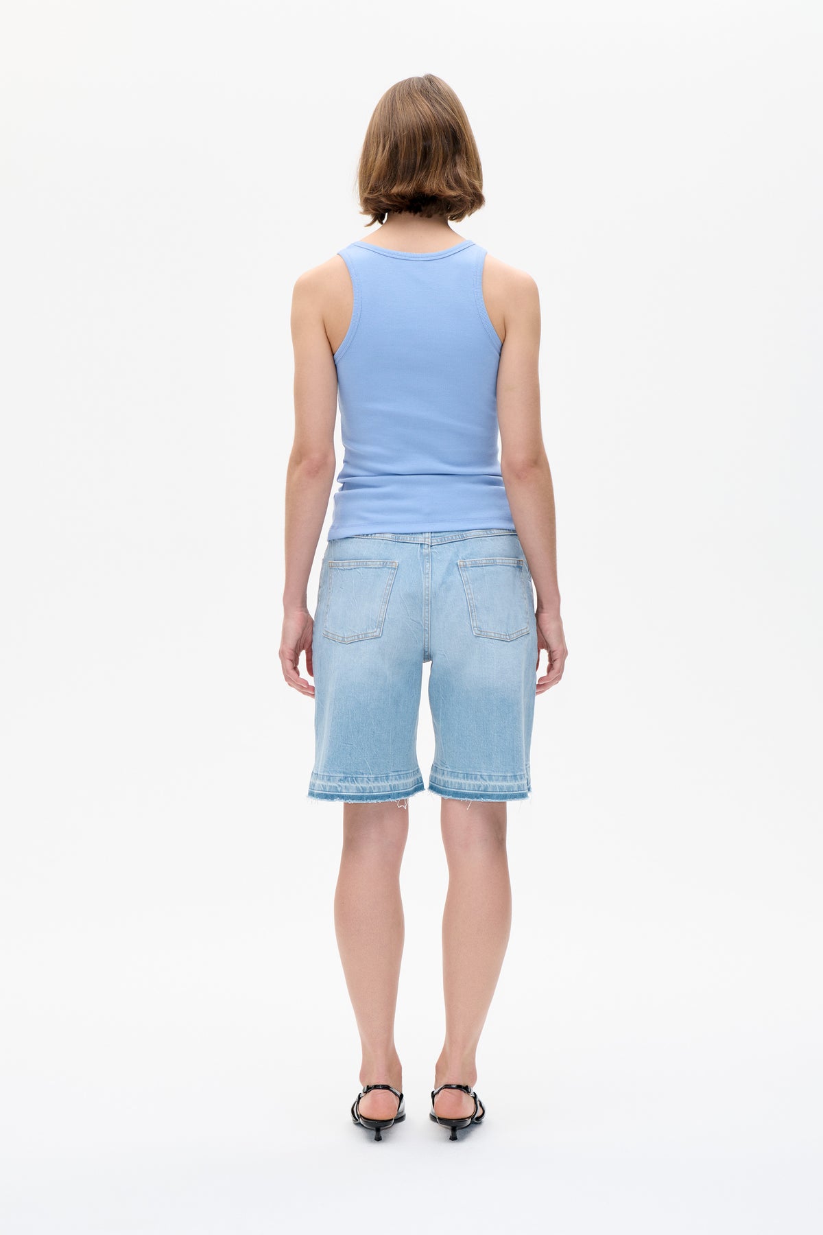 Back view of a light blue ribbed sleeveless tank top with pale blue denim shorts, patch pockets and frayed hems.