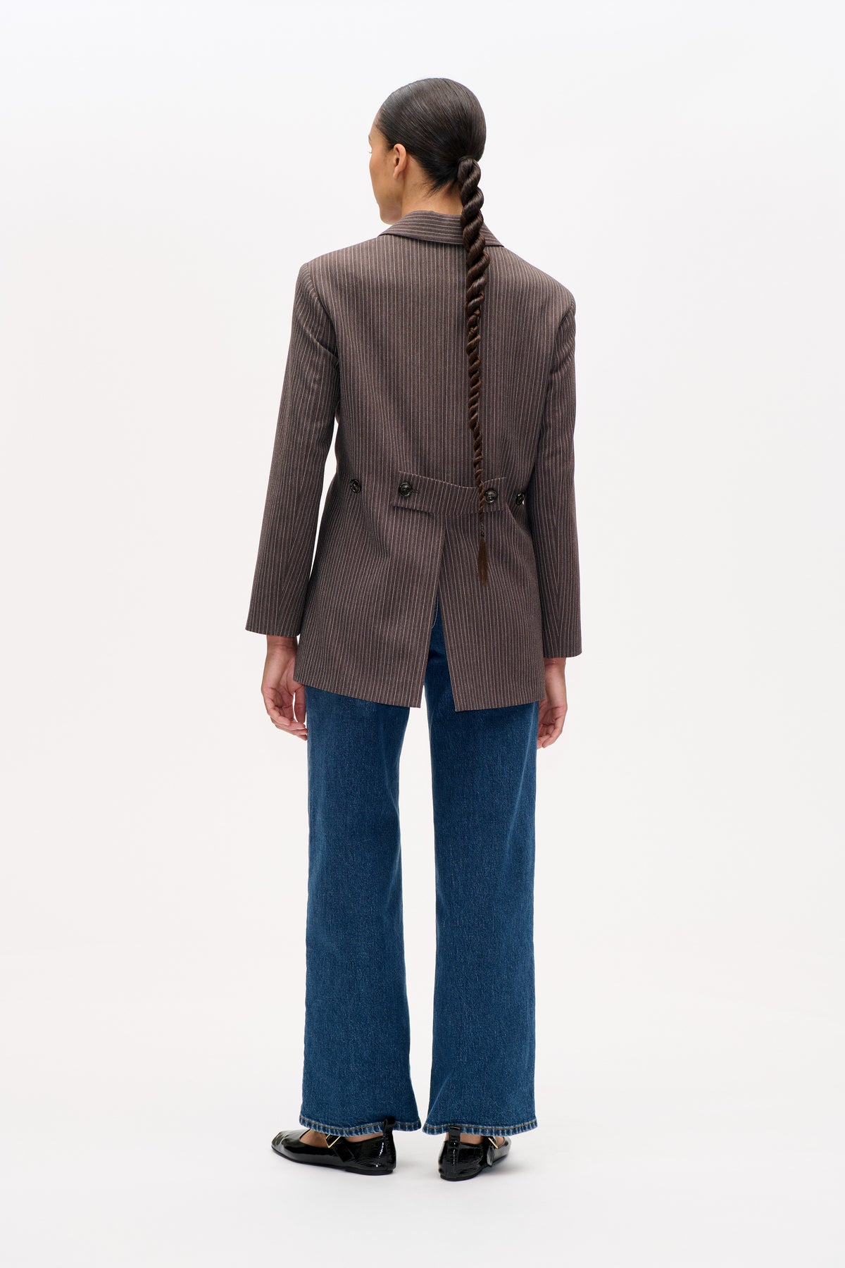Back view of a brown pinstripe blazer with a buttoned waist tab, styled with wide-leg blue jeans.