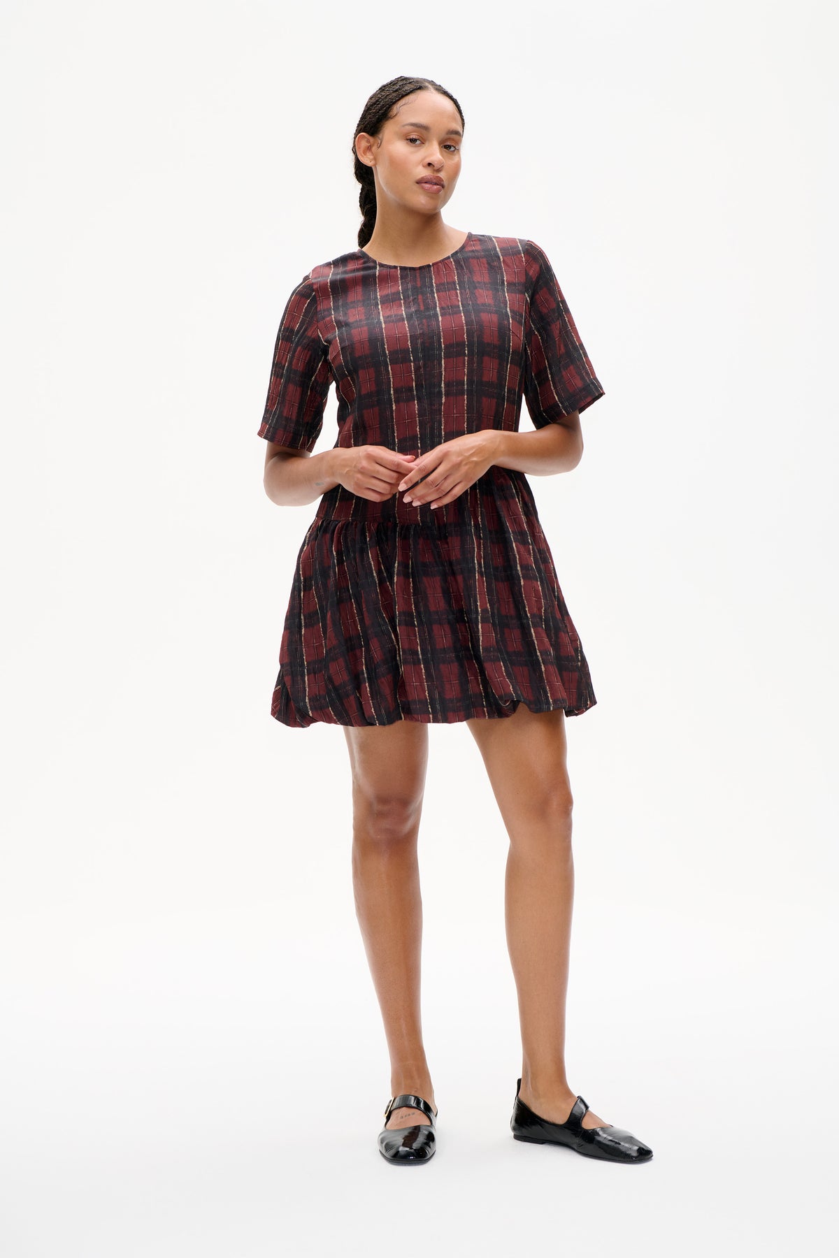 Model wearing a burgundy and black plaid short-sleeved dress with a gathered skirt, shown from the front against a white background.