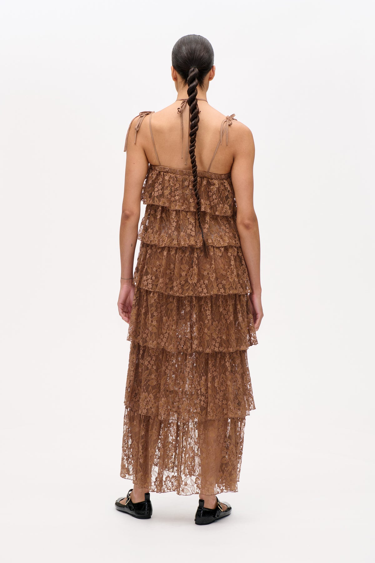 Back view of a model wearing a brown floral lace tiered dress with thin tie straps and an open back.