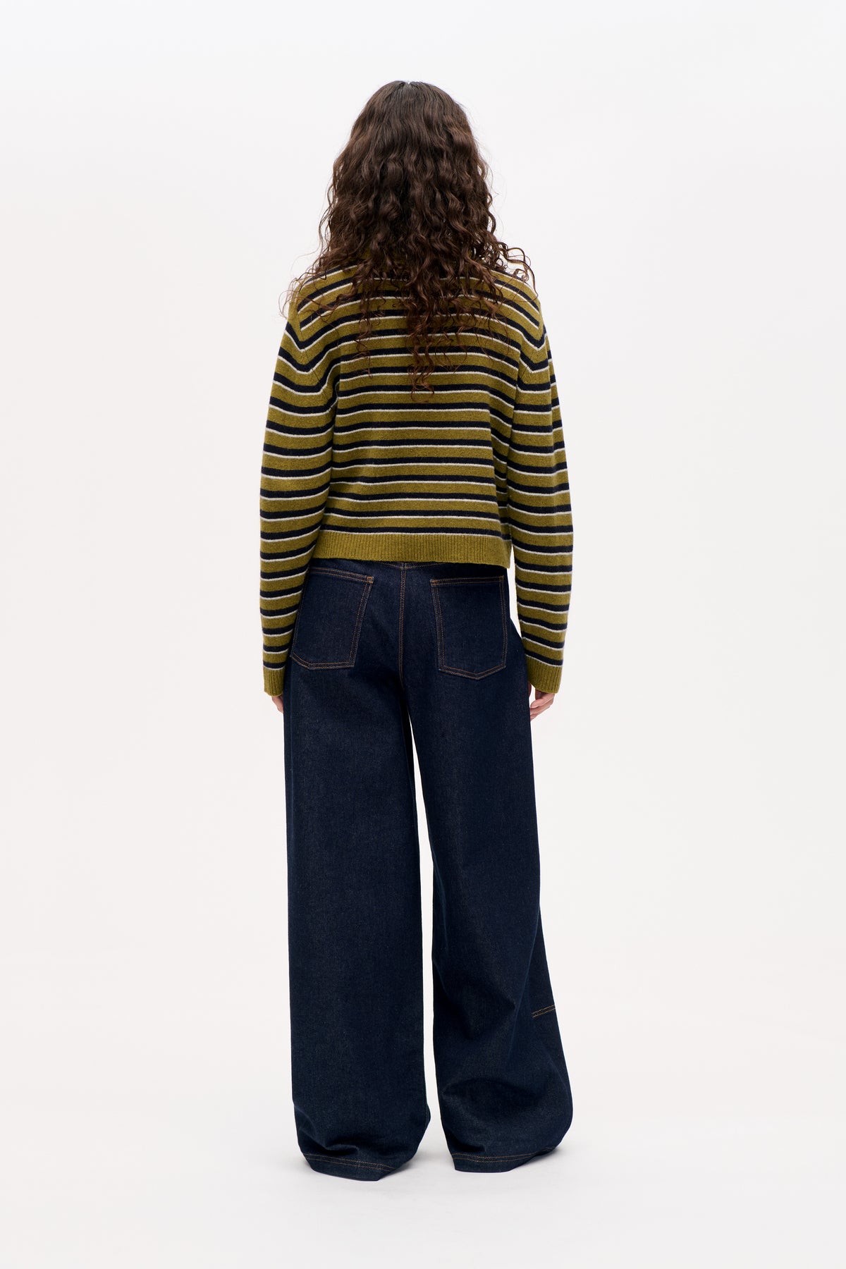 Vue de dos d'un mannequin portant un pull à rayures olive, bleu marine et blanc et un jean large foncé.