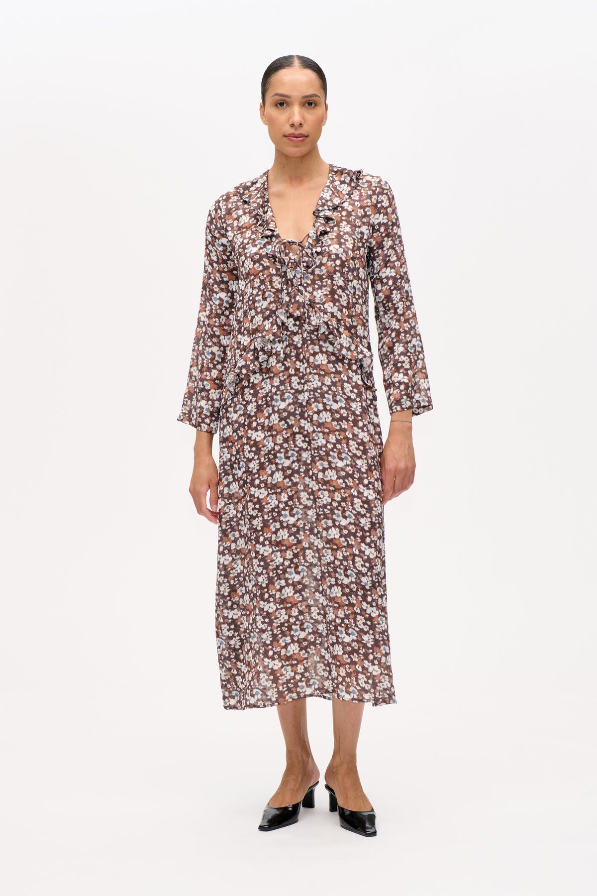 Front view of a model wearing a brown floral-print midi dress with long sleeves, a ruffled V-neckline and ruffle trim.