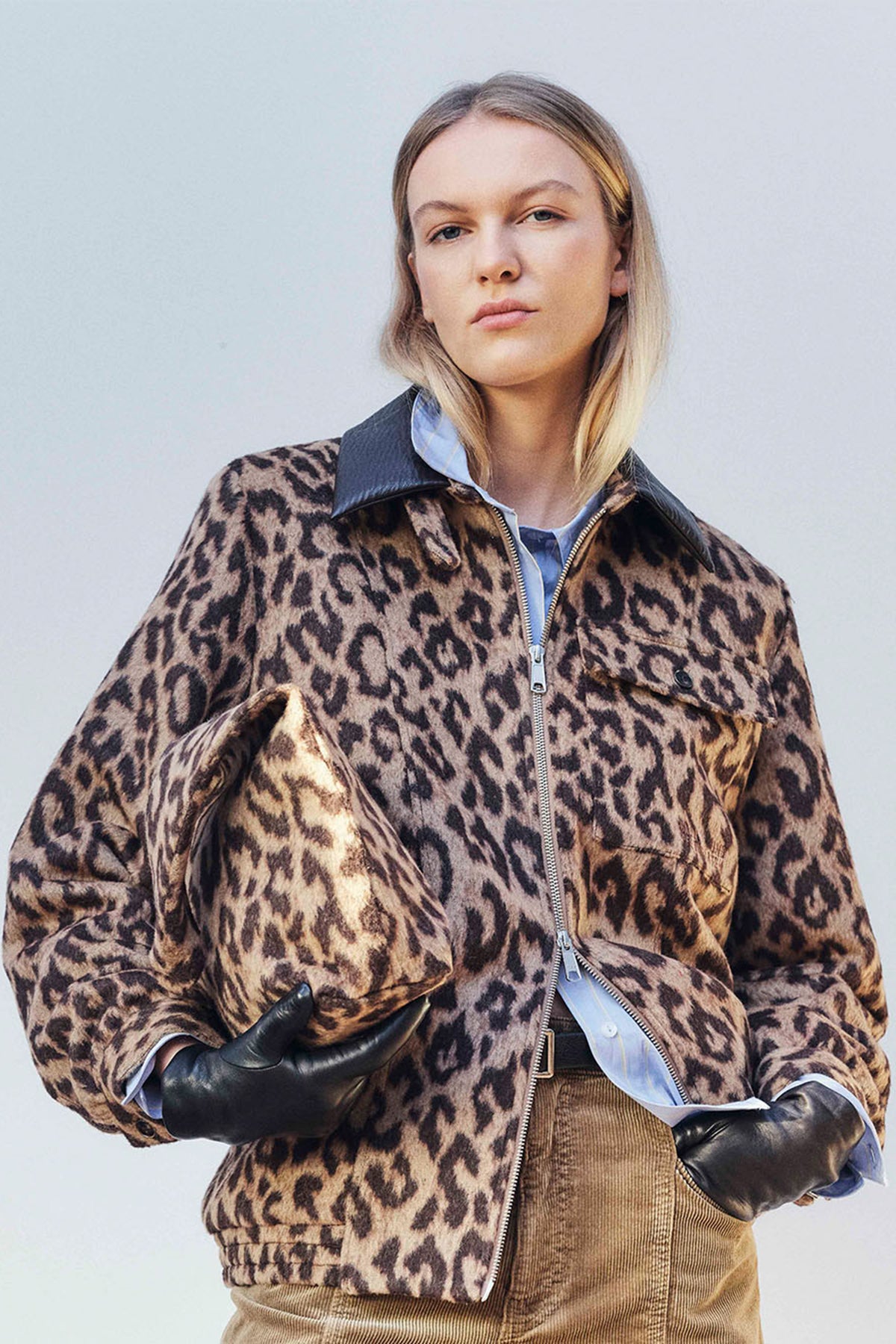 Campagneportret van een jas met luipaardprint in bruin en zwart en rits voorop, gedragen over een blauwe blouse en een bruin geribd topje.