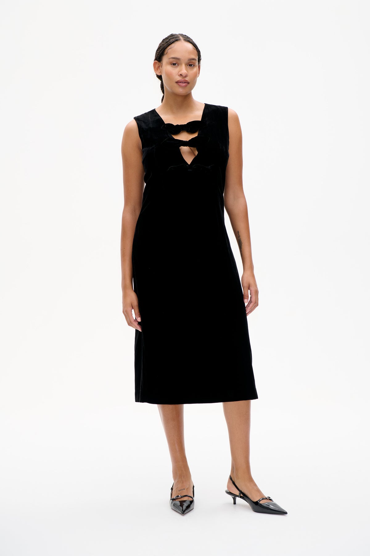 Front view of a black sleeveless knee-length dress with bow-shaped chest details and cutout openings.
