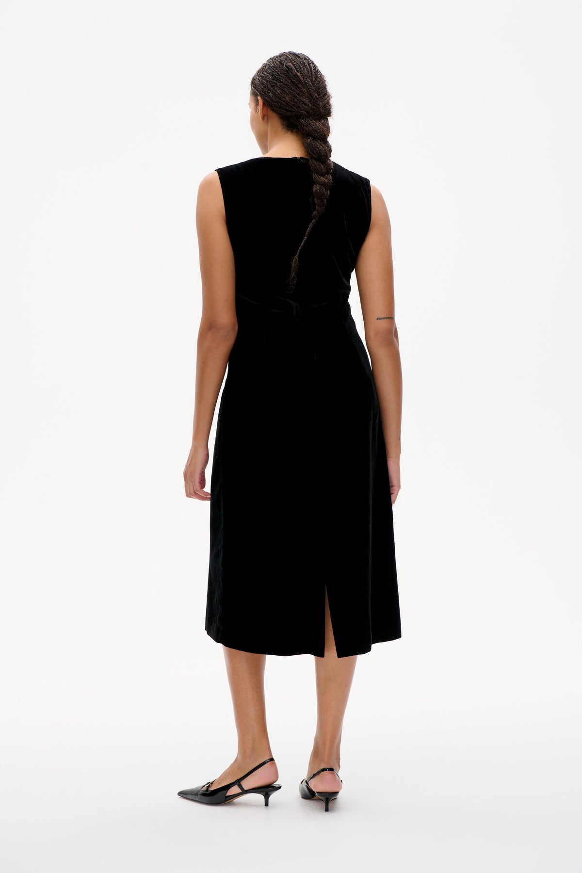 Back view of a model wearing a black sleeveless midi dress with a straight silhouette and rear slit.