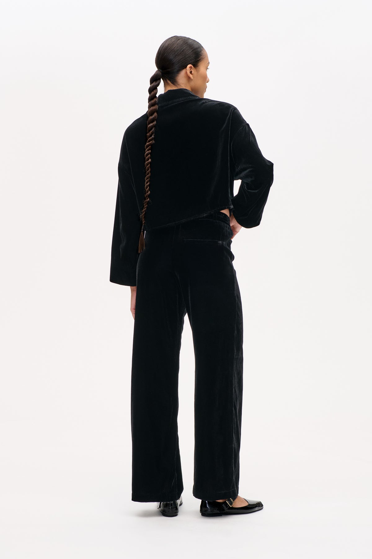 Back view of a model wearing a black velvet jacket and matching wide-leg trousers.