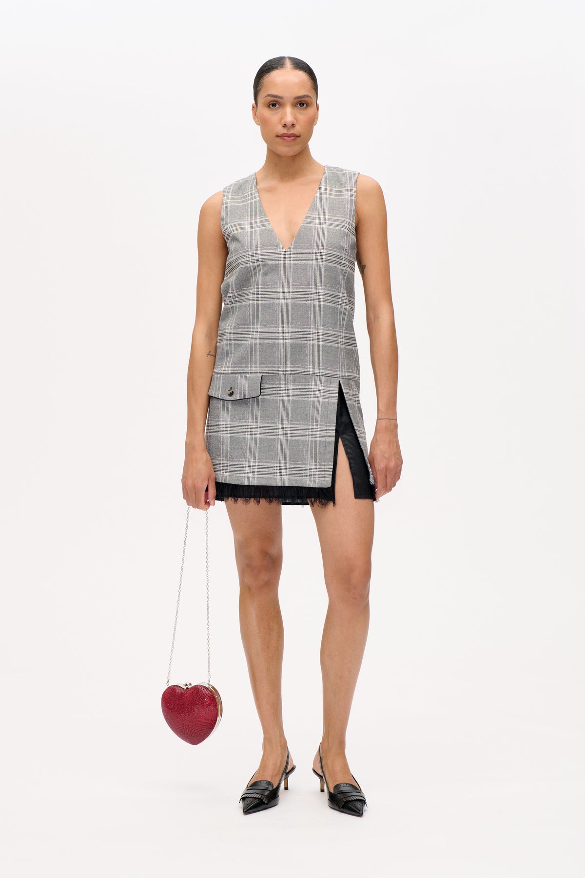 Front view of a model wearing a grey plaid sleeveless V-neck mini dress with a flap pocket, side slit and black lace hem.