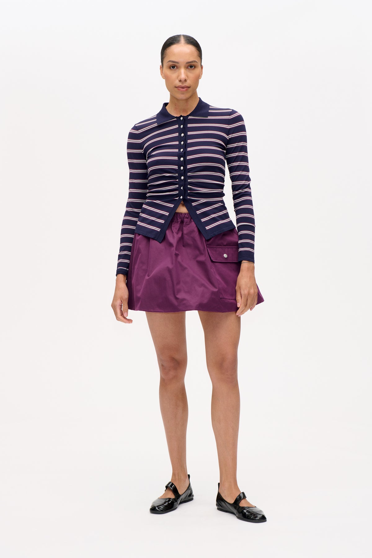 Front view of a model wearing a navy collared cardigan with cream and burgundy stripes, paired with a plum mini skirt.