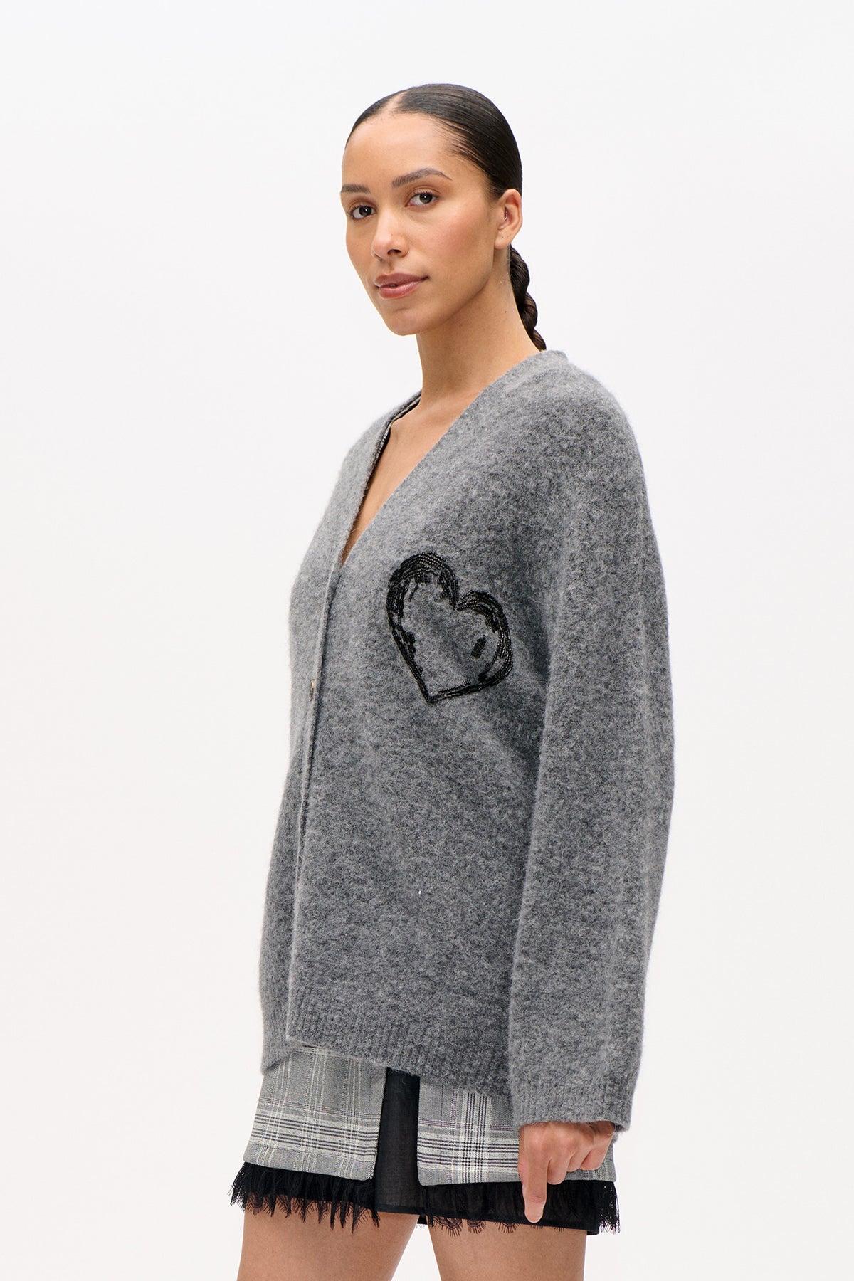 Close-up front view of a grey knit cardigan with a black heart motif, layered over checked shorts with black lace trim.