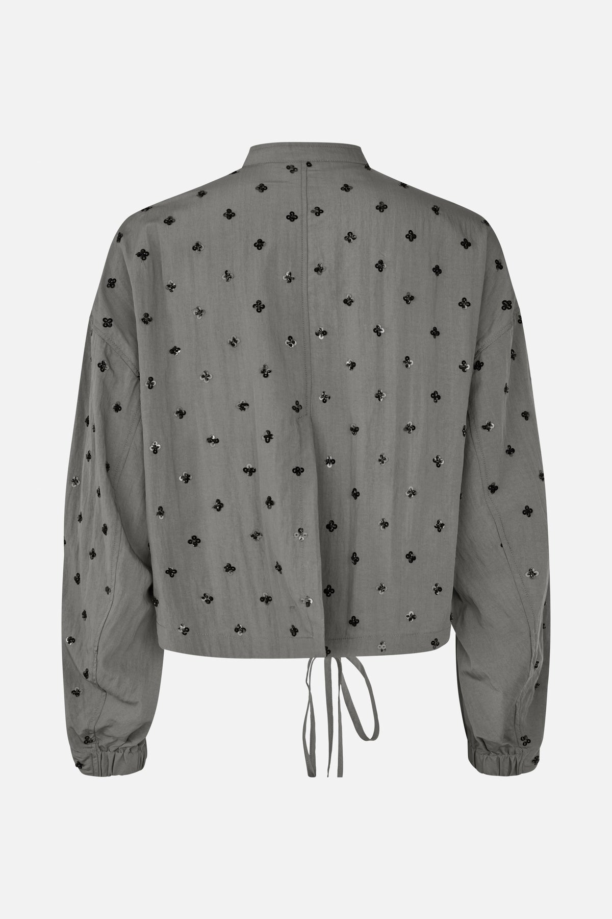 Back view of a grey long-sleeved collared shirt with scattered black floral embellishments, elastic cuffs and a drawstring hem.