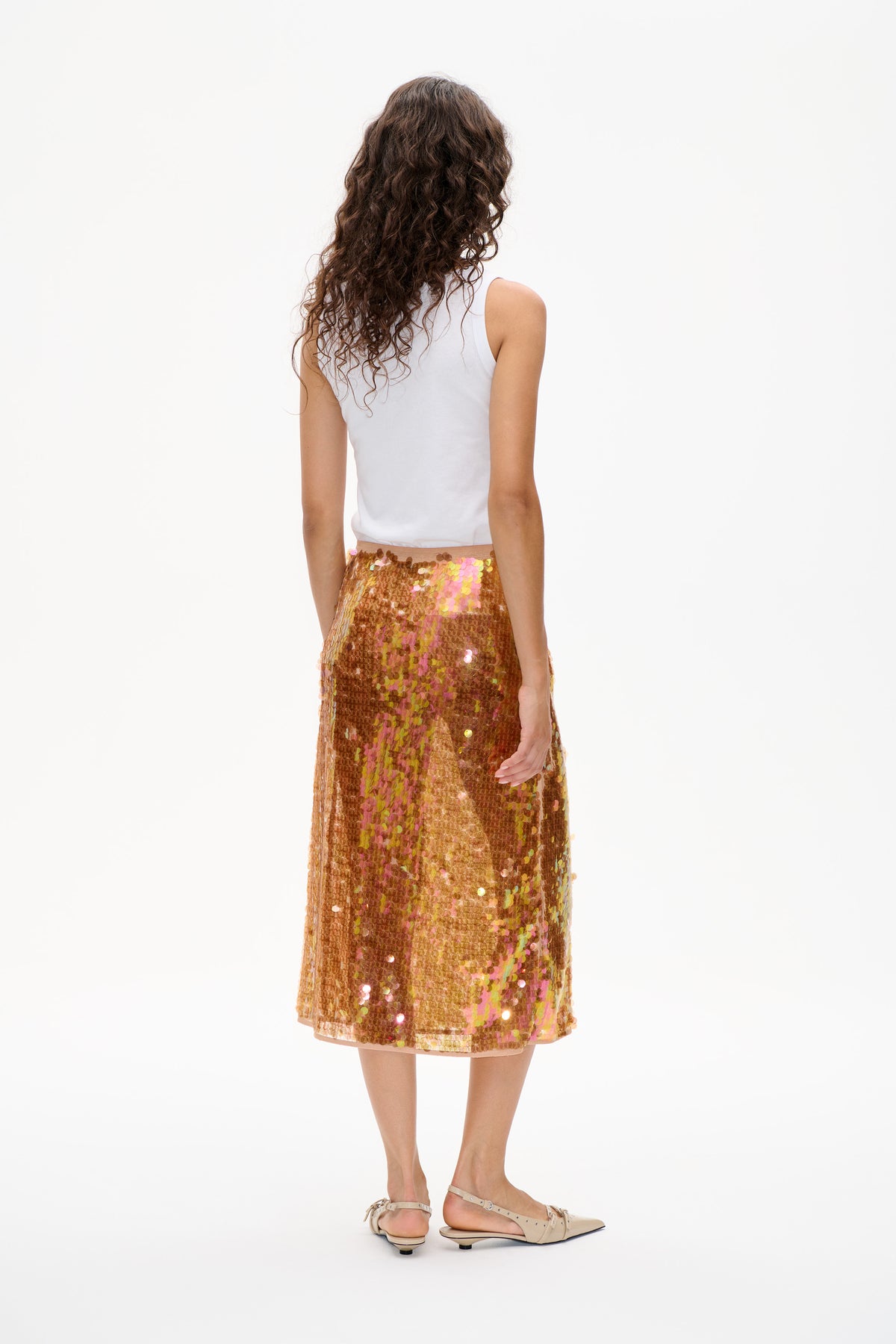 Back view of a model wearing a white sleeveless top, an iridescent bronze sequin midi skirt and beige pointed flats.