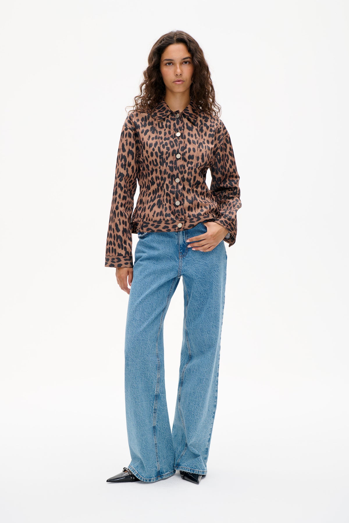 Model trägt eine Jacke mit braun-schwarzem Leopardenmuster, Knopfleiste und spitzem Kragen sowie blaue Jeans mit weitem Bein.