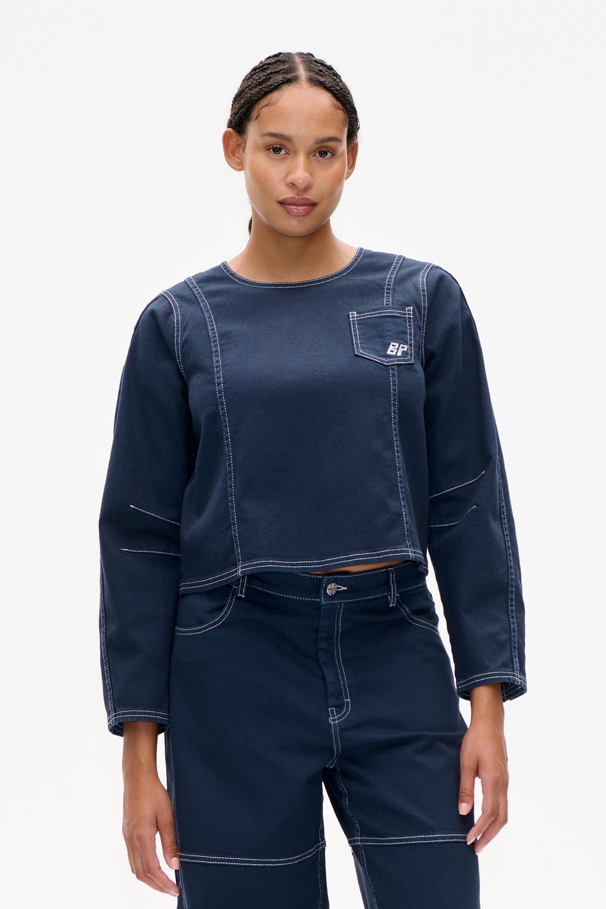 Front view of a dark indigo long-sleeved top with contrast white stitching, panel seams and a chest pocket, paired with matching trousers.