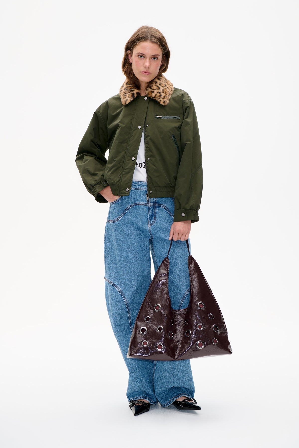 Model wearing an olive green jacket with a tan-and-black leopard-print collar, front zipper and snap closures, paired with blue jeans.