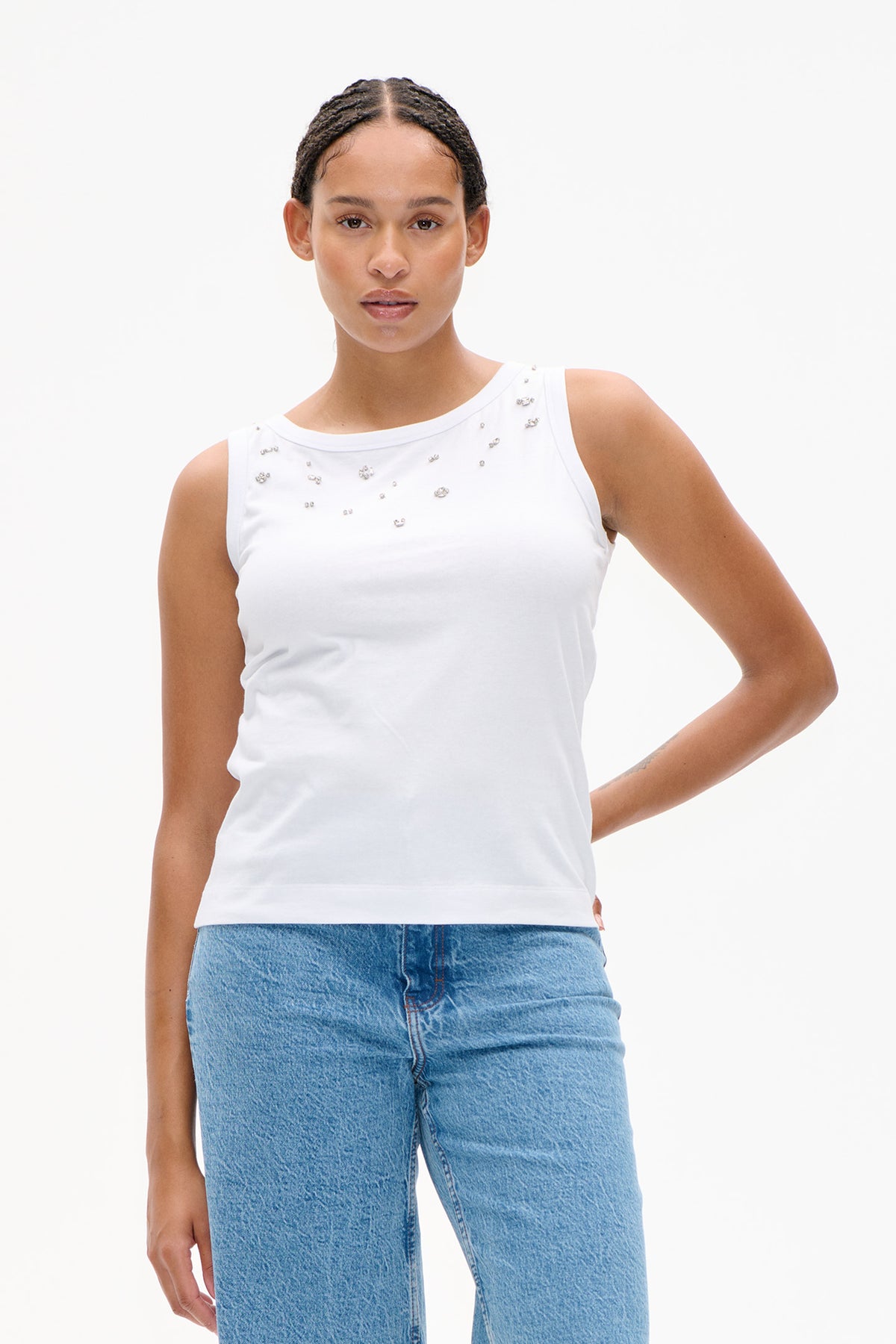 Front view of a white sleeveless top with scattered silver embellishments, paired with light blue jeans.