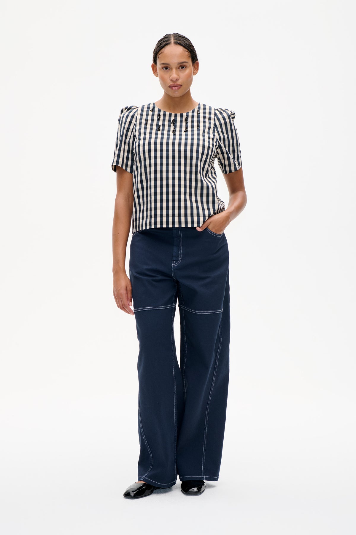 Model wearing a navy-and-cream checked top with puffed shoulders, short sleeves and black bead embellishments, paired with wide-leg navy trousers.