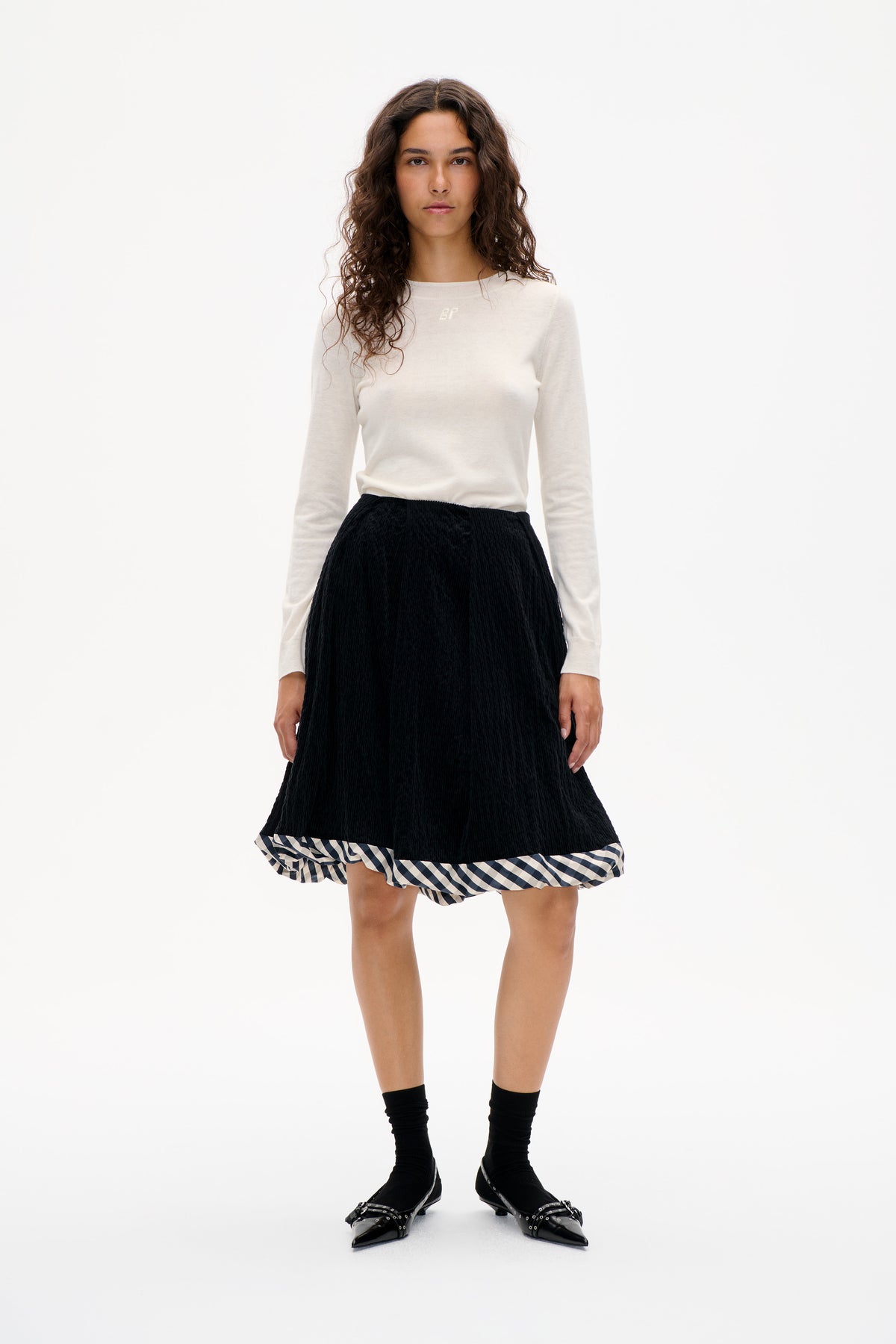 Front-facing model in an ivory long-sleeved top and black textured skirt with a black-and-cream checked ruffle hem.