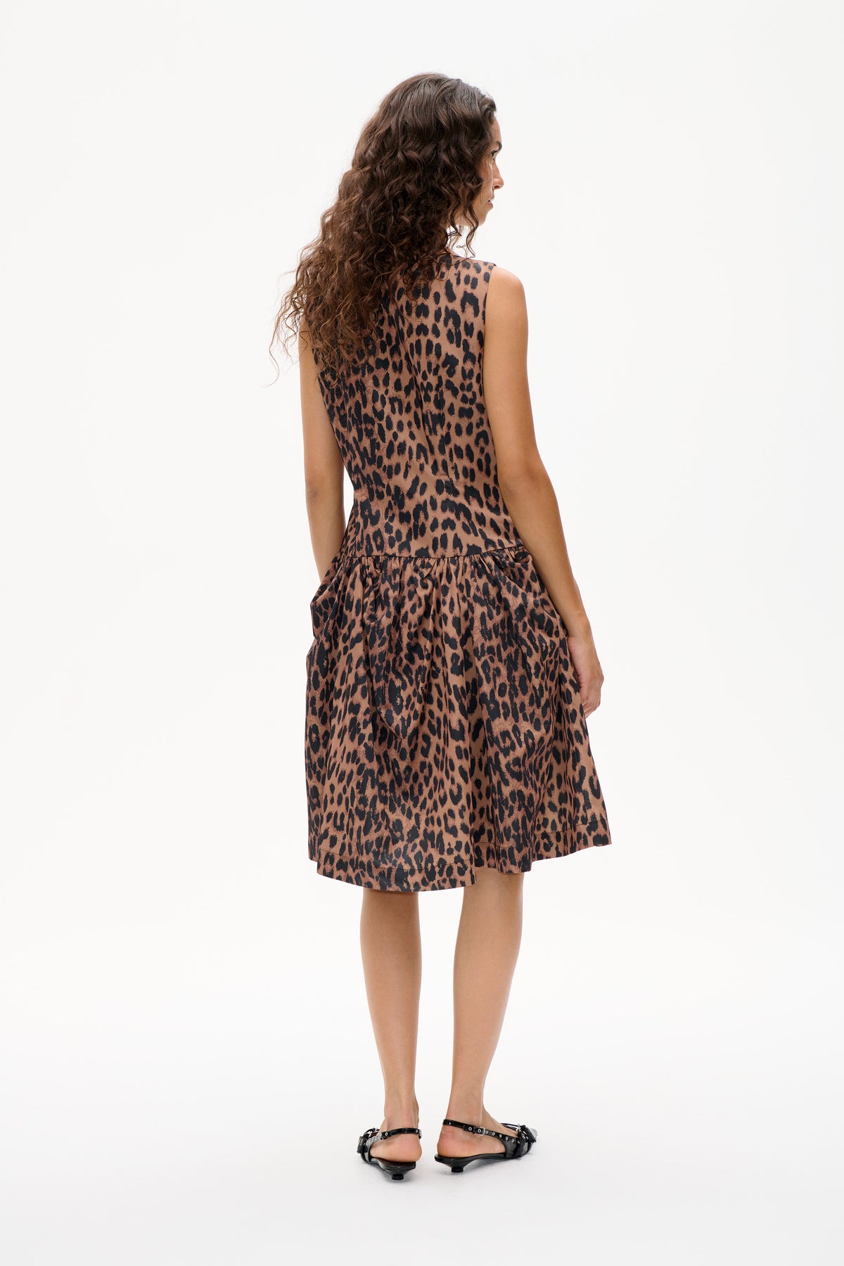 Model viewed from behind wearing a sleeveless brown-and-black leopard-print dress with a gathered skirt.