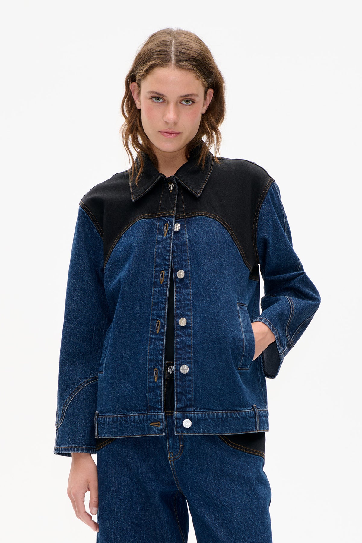 Front view of a blue denim jacket with a black contrast yoke and collar, contrast stitching, and silver-tone buttons.
