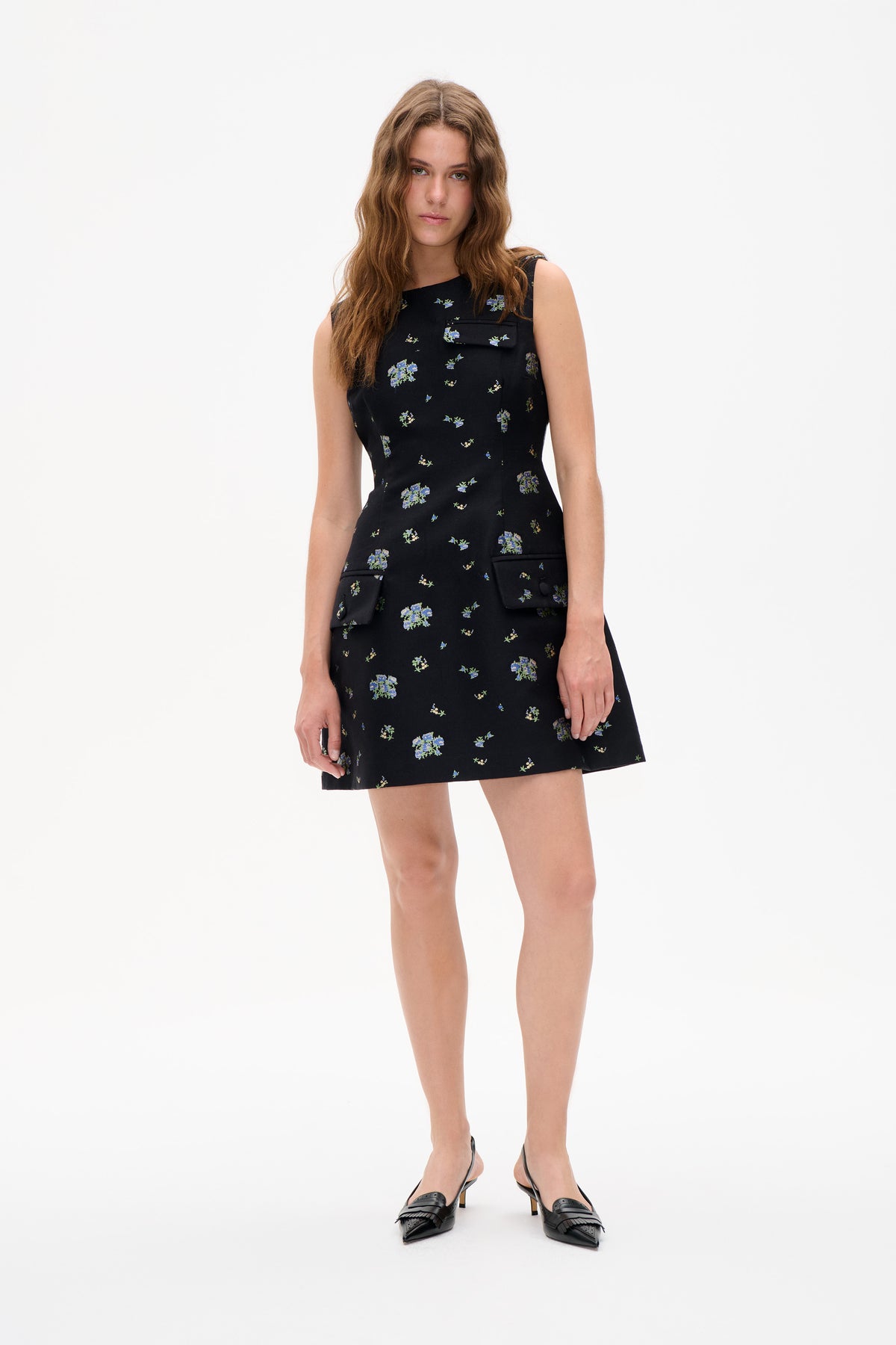 Model wearing a black sleeveless mini dress with scattered blue and green floral print and flap pockets, shown from the front.