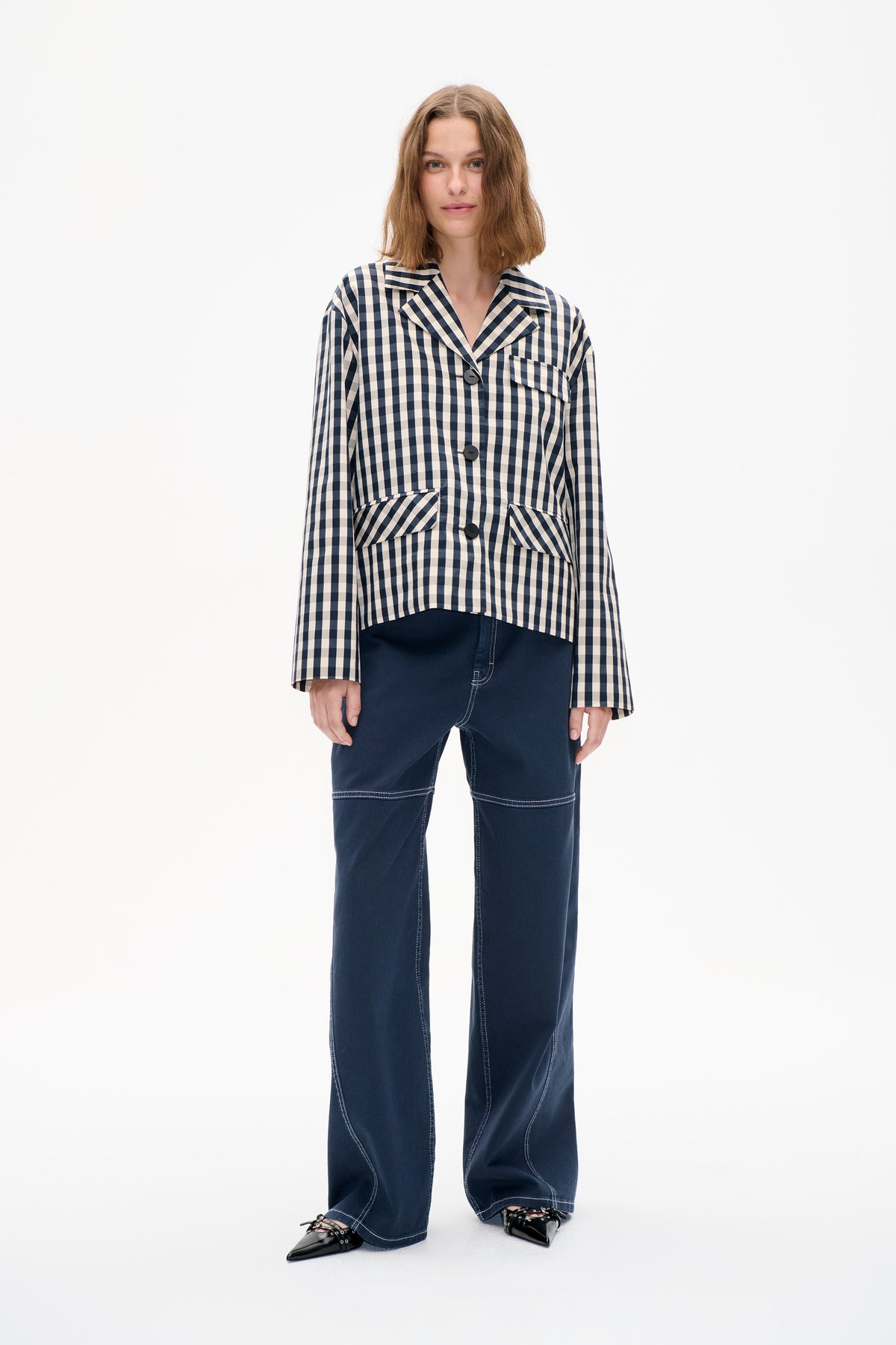 Front view of a model wearing a navy and cream checked button-front jacket with lapels and patch pockets, paired with dark wide-leg jeans.