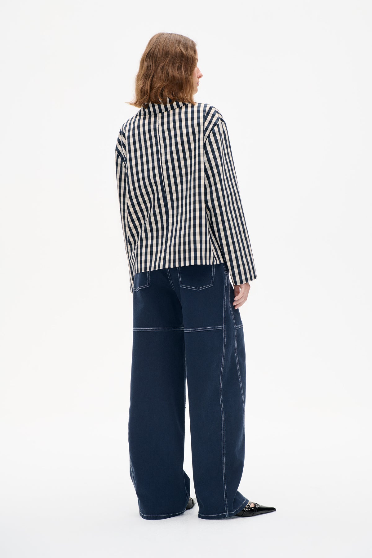 Back three-quarter view of a model wearing a navy and cream checked long-sleeved shirt with dark wide-leg jeans.